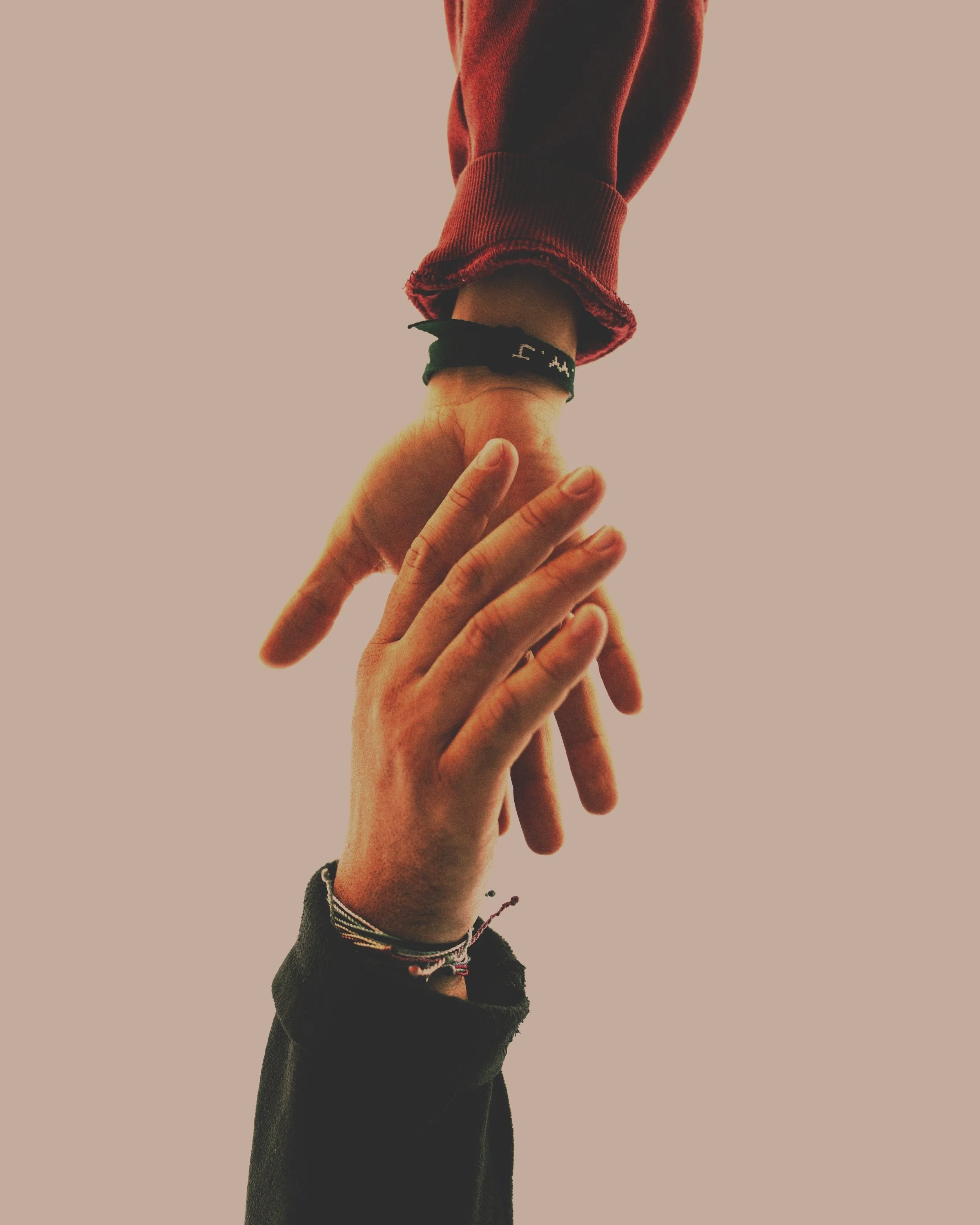 Deux mains qui se touchent, une main féminine avec plusieurs bracelets, l'autre masculine, fond clair