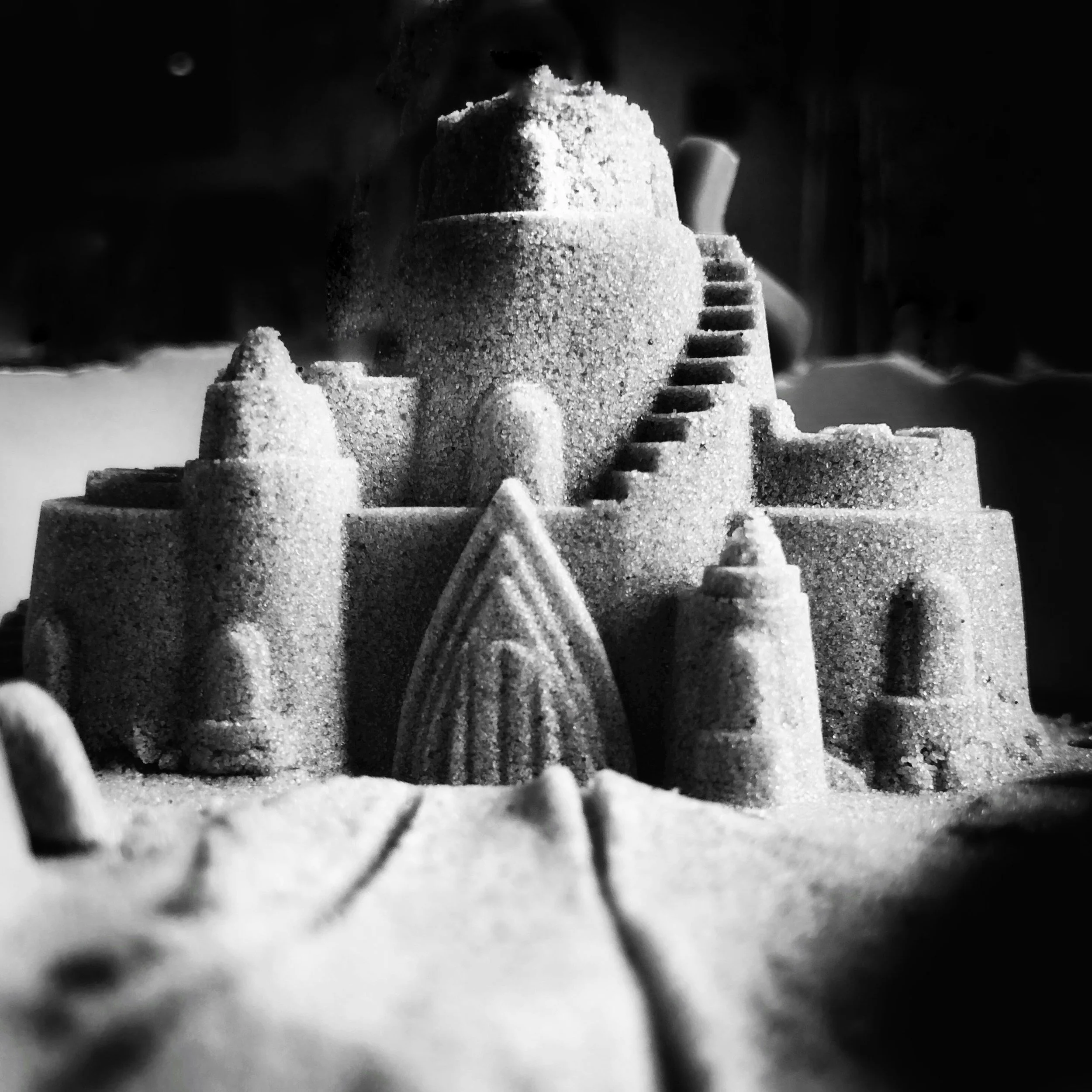A detailed sandcastle sculpture with multiple towers, a large central dome, and an arched gate, decorated with textured sand, on a sandy surface.