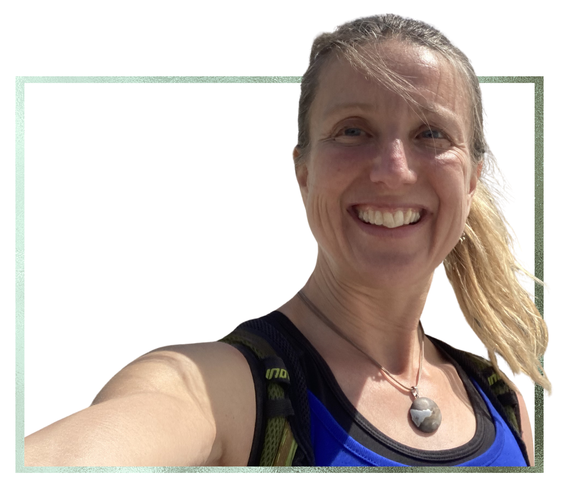 Close-up of smiling woman with blond hair, wearing a blue top and a necklace, taking a selfie outdoors under sunlight.