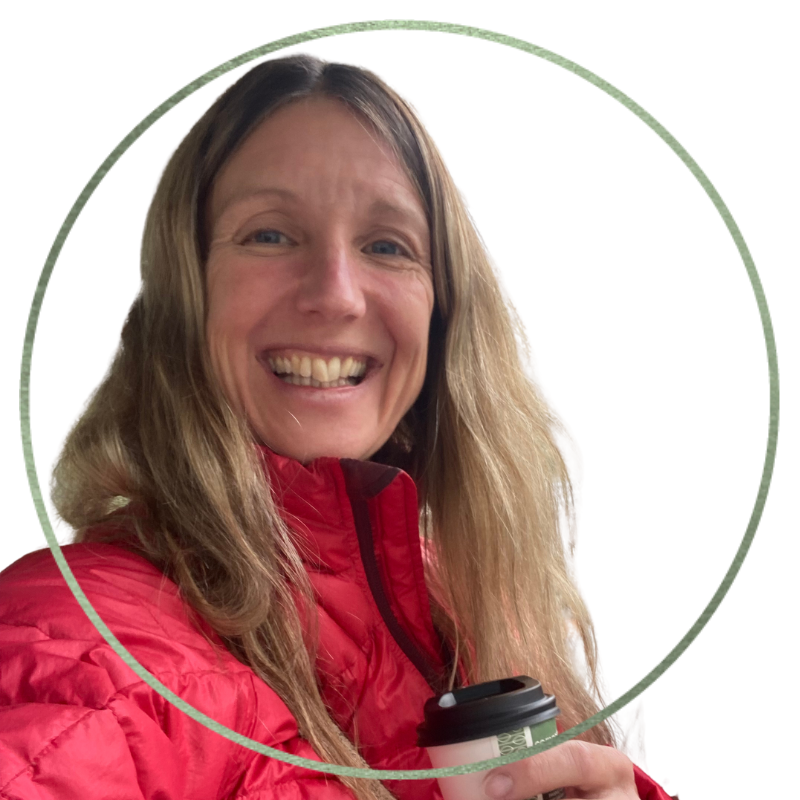 Smiling woman with long blonde hair wearing a red jacket, holding a coffee cup.