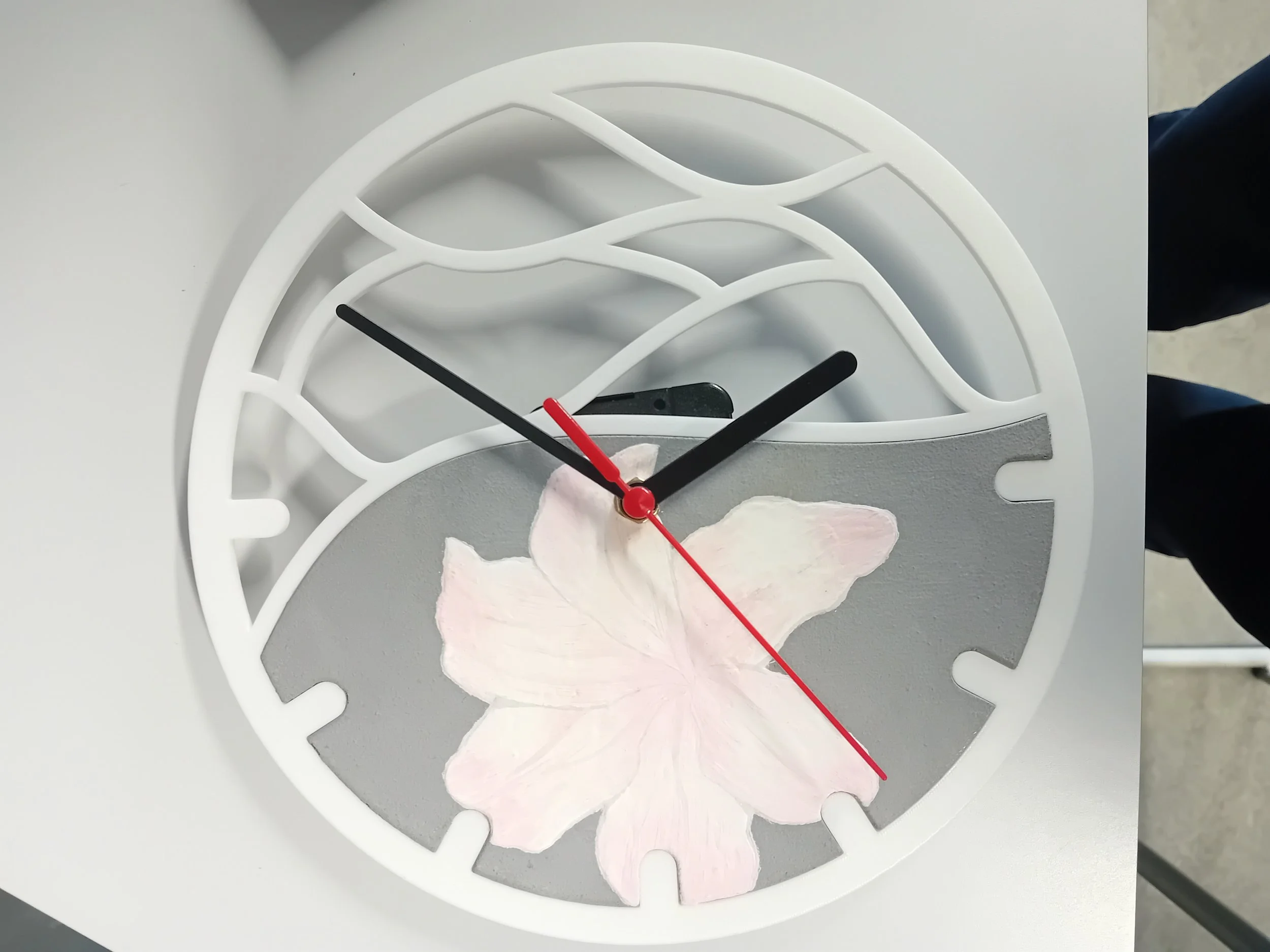Decorative round clock with a white frame, black hour and minute hands, a red second hand, a gray background, and a light pink flower design.