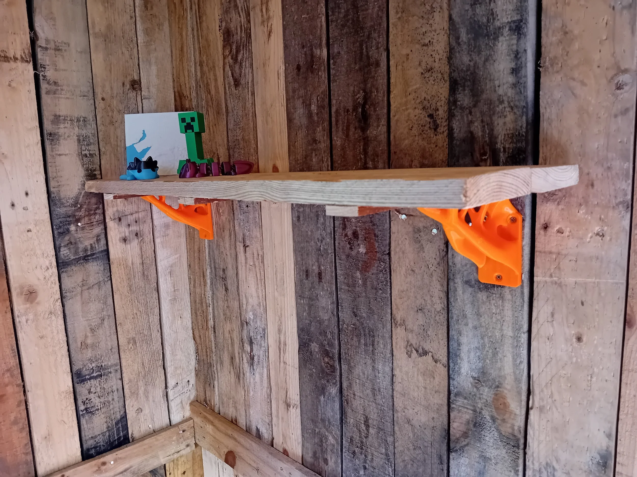 A wooden shelf mounted on orange brackets, with Minecraft-themed toys and decor, inside a room with wooden plank walls.