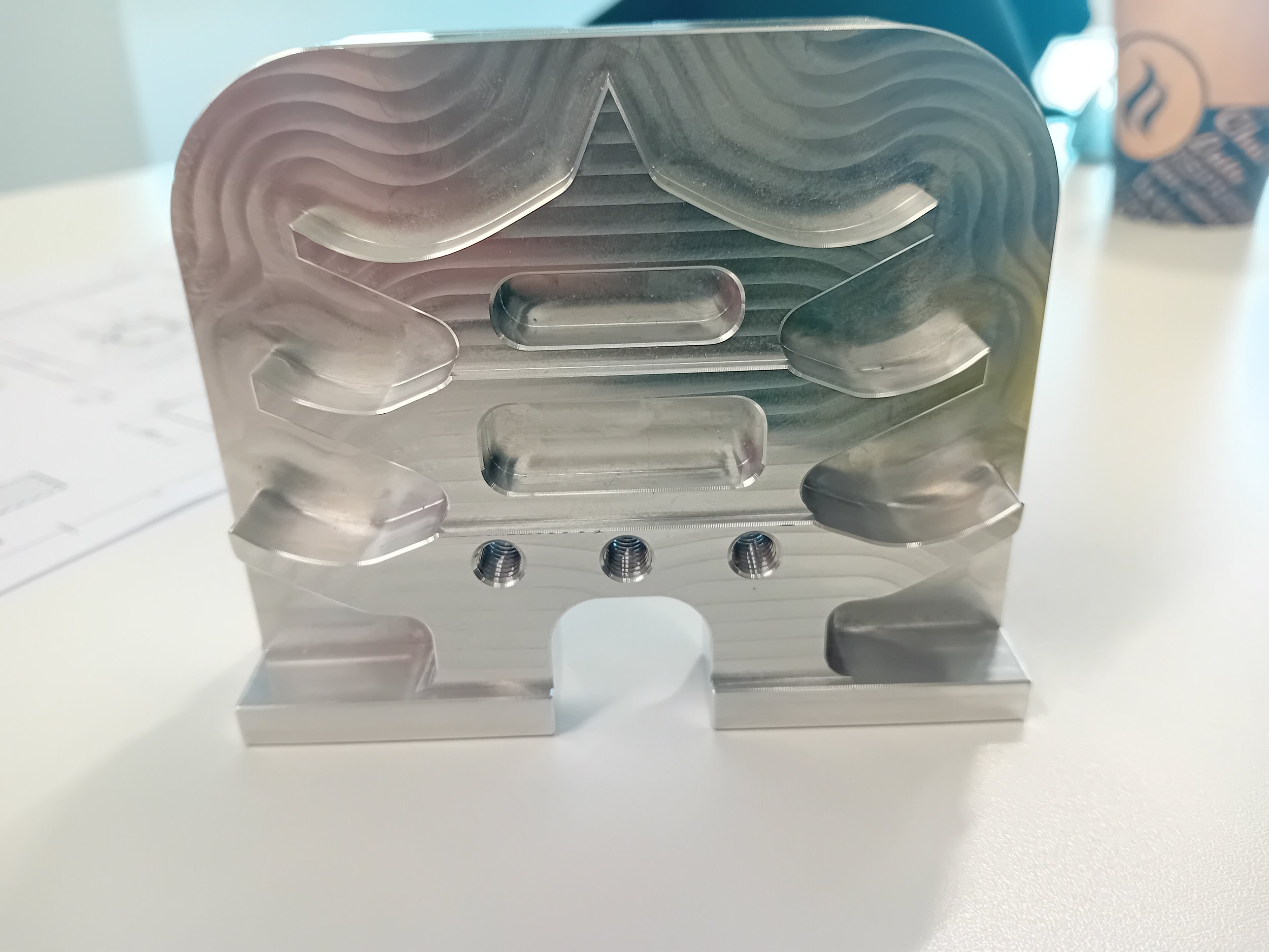 Close-up of a metallic metallic object with grooves and threaded holes on a white surface.