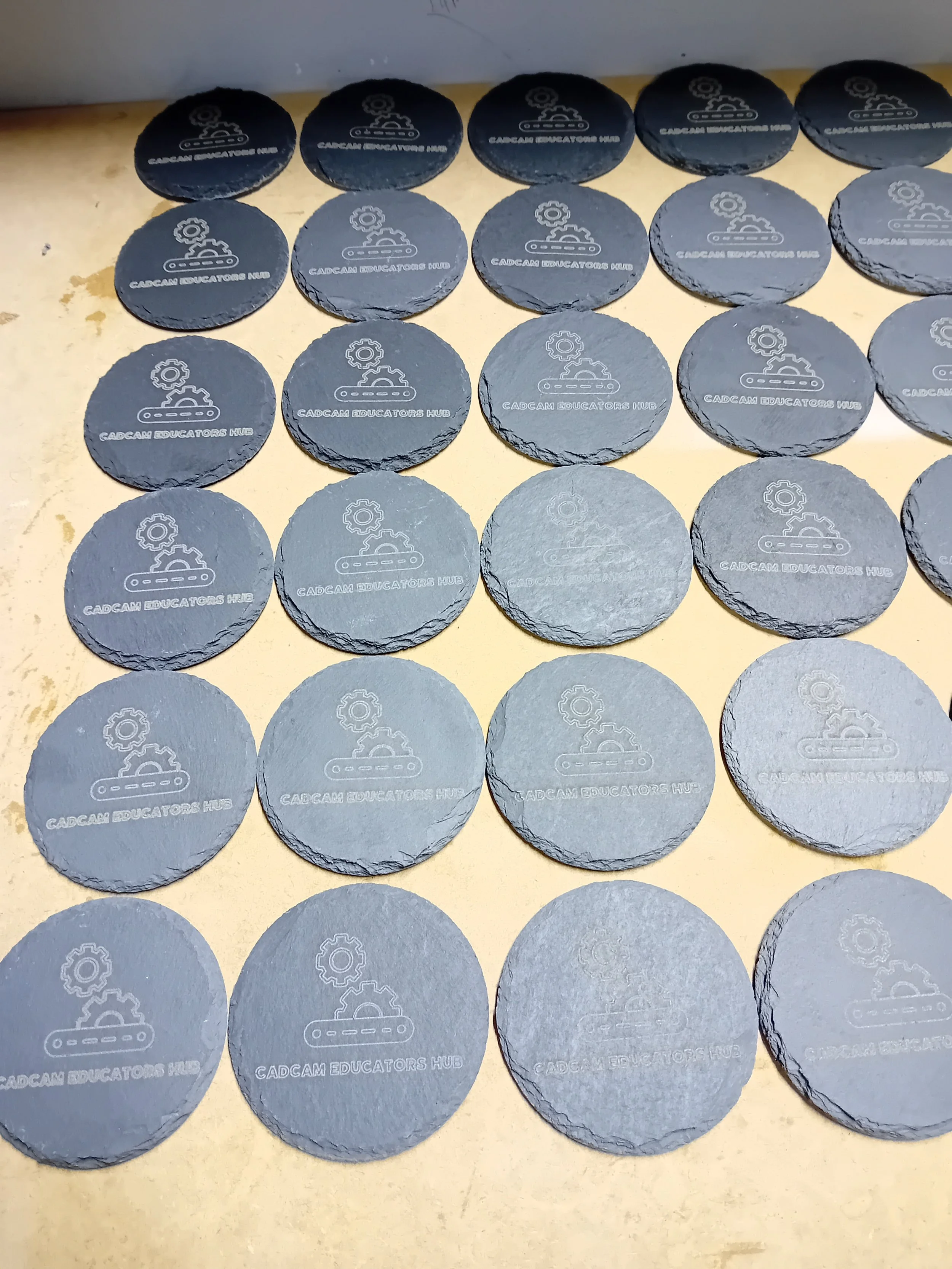 Multiple round black tokens with the logo of a gear and conveyor belt, labeled 'CADCAM EDUCATORS HUB.'