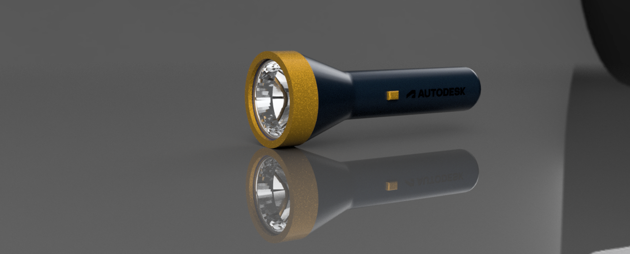 A black flashlight with a gold rim and a gold Autodesk logo on the handle, lying on a gray reflective surface.