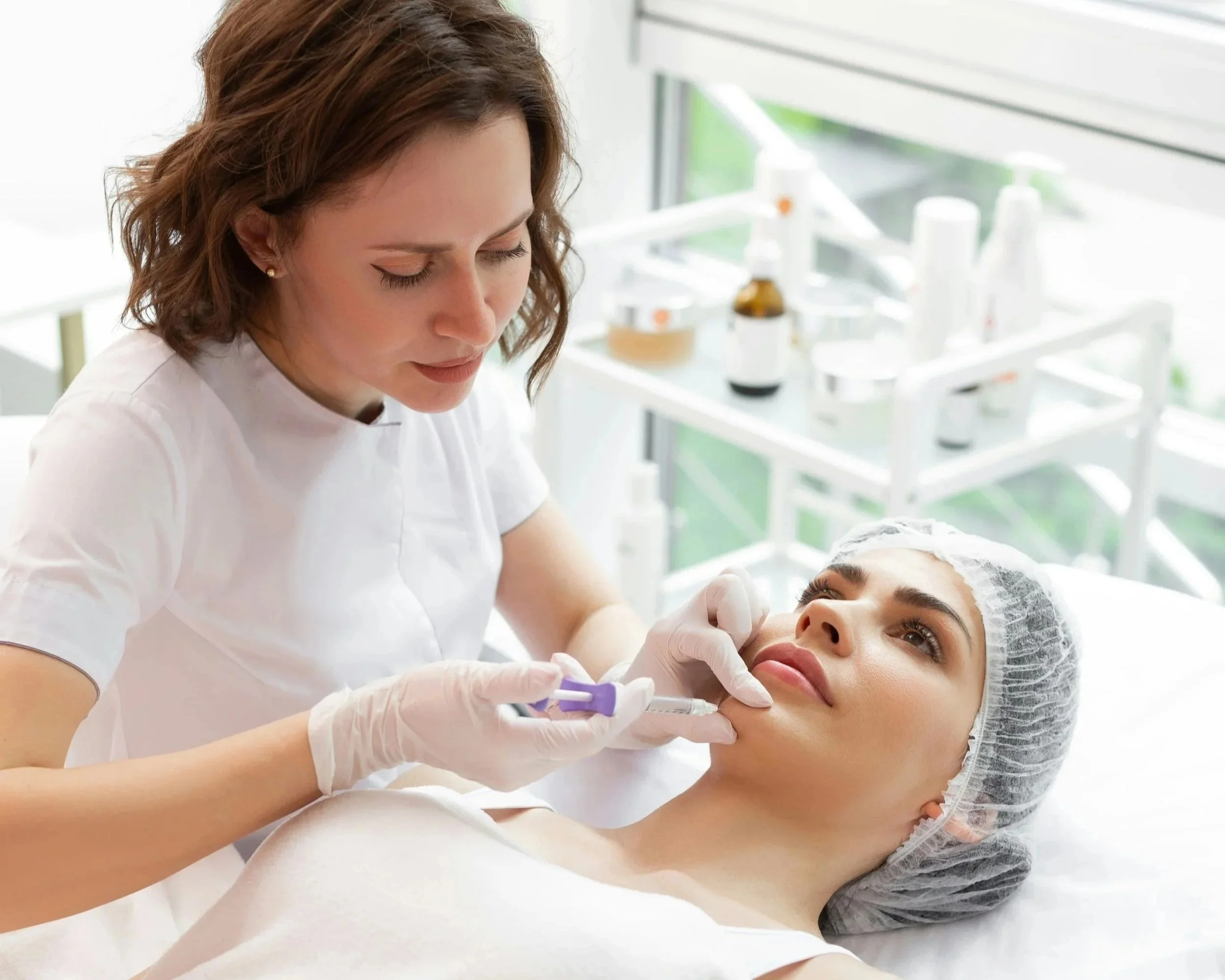 A woman receiving a cosmetic injection in her lips from a healthcare professional in a clinical setting.