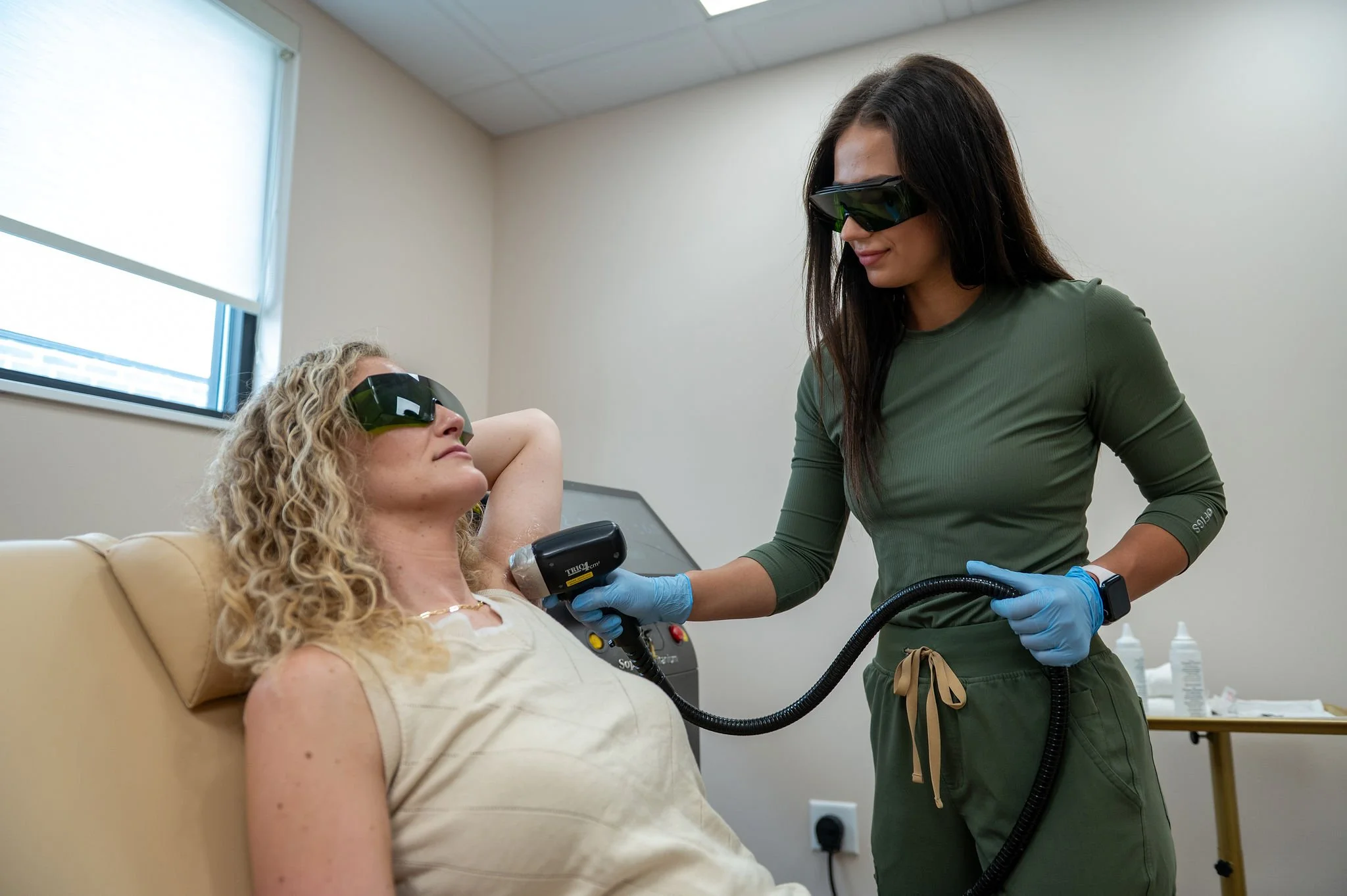 A person using a laser hair removal device on their underarm with a gloved hand, showing the device emitting laser pulses.
