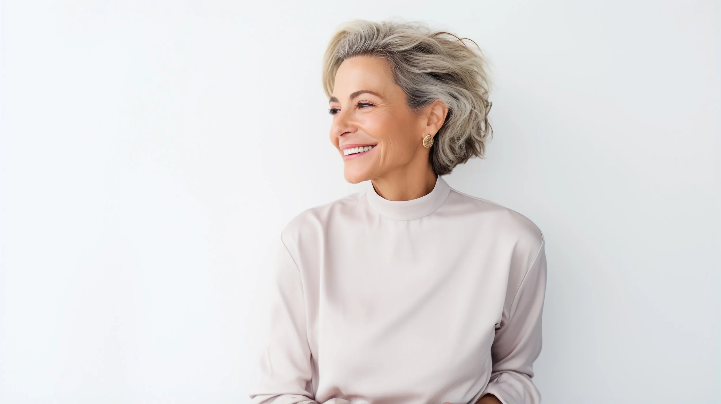 Smiling older woman with short gray hair, wearing a white blouse and gold earrings, looking to her right against a plain white background.