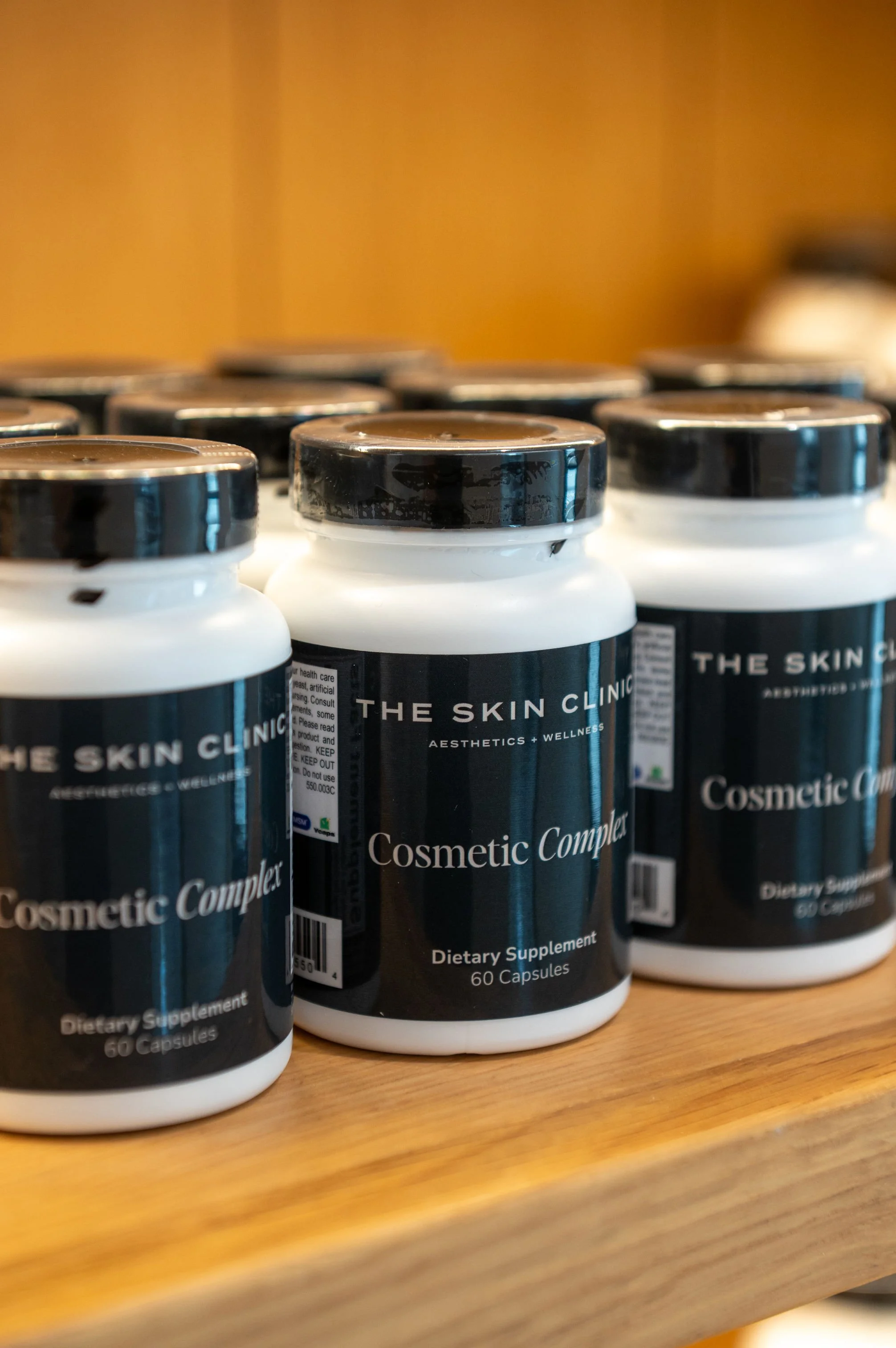 Multiple bottles of dietary supplement labeled 'The Skin Clinic' on a wooden surface