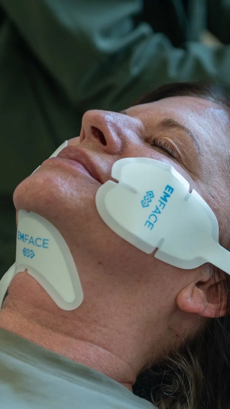 A woman receiving a facial treatment with EMFACE, a device that uses electrical muscle stimulation on her face and neck.