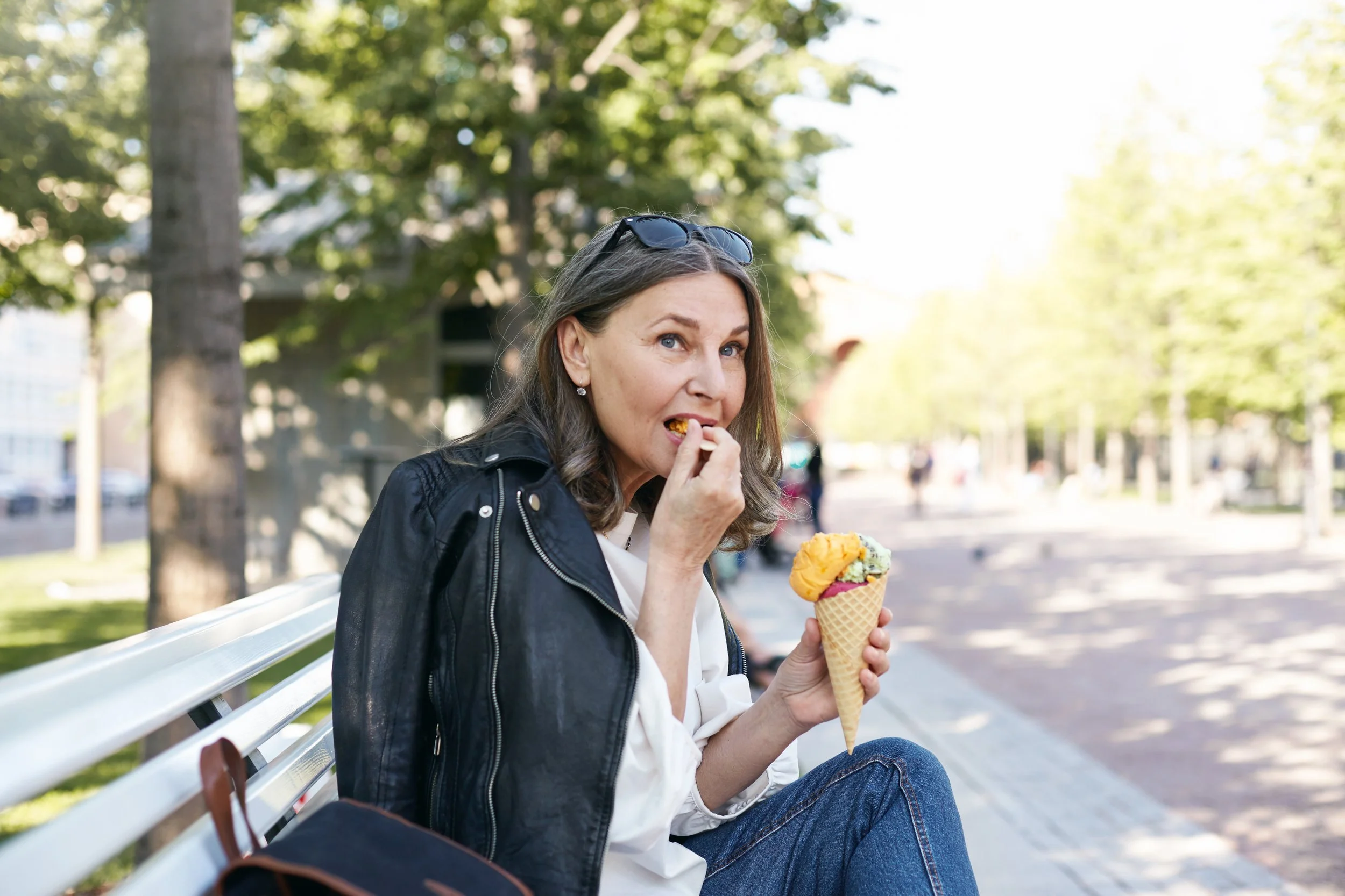 A woman sitting on a park bench eating ice cream cone on a sunny day