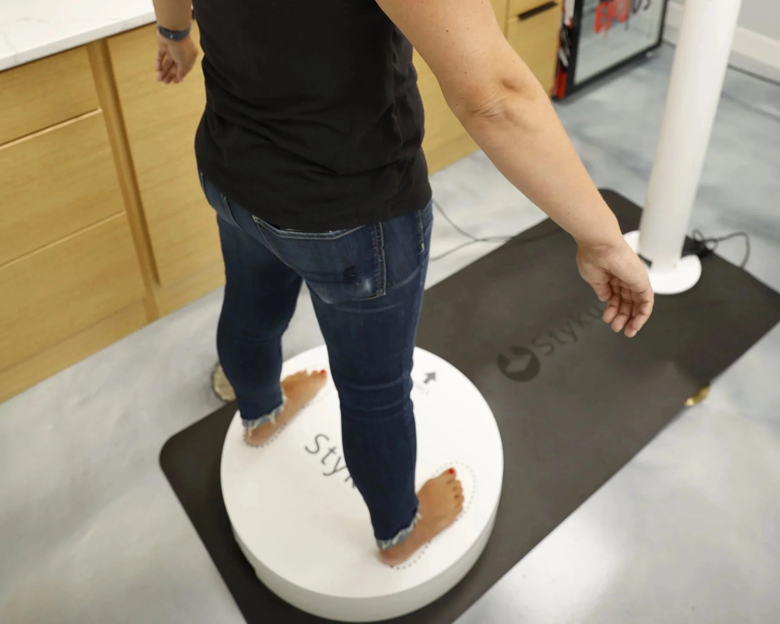 Person standing on a circular floor graphic that has text and footprints, in a room with wooden cabinets and a white pole.