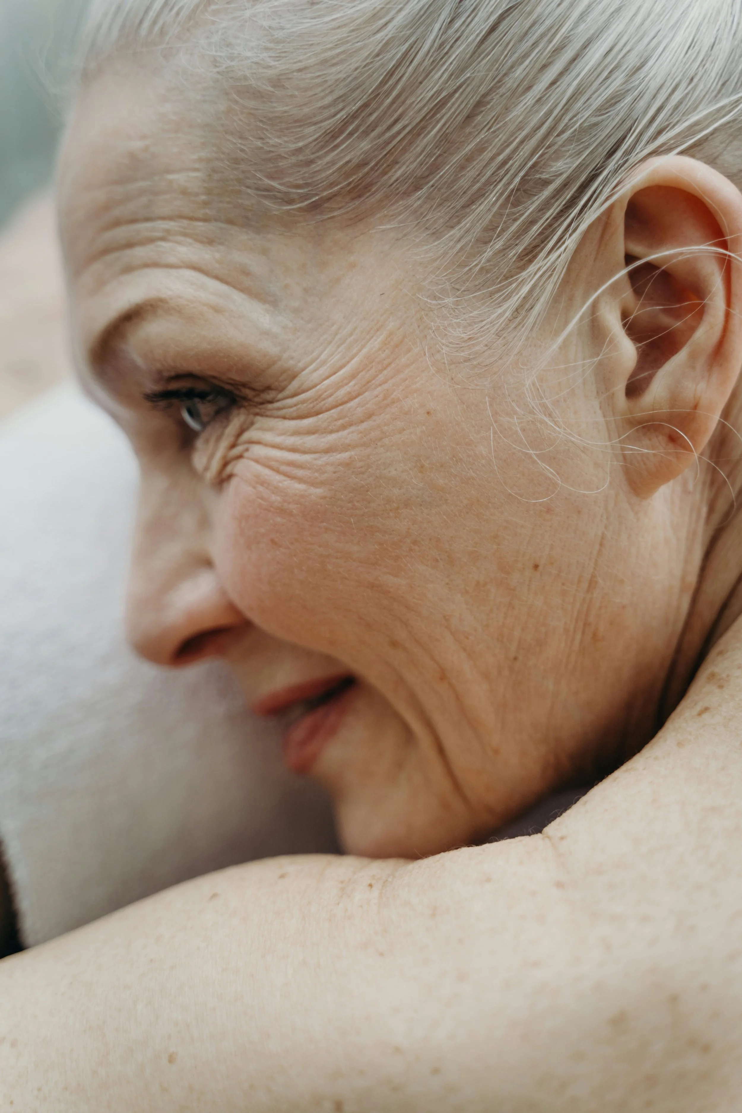Close-up of an elderly woman's face resting on her arm, showing her smiling eye, wrinkles, and light-colored hair.