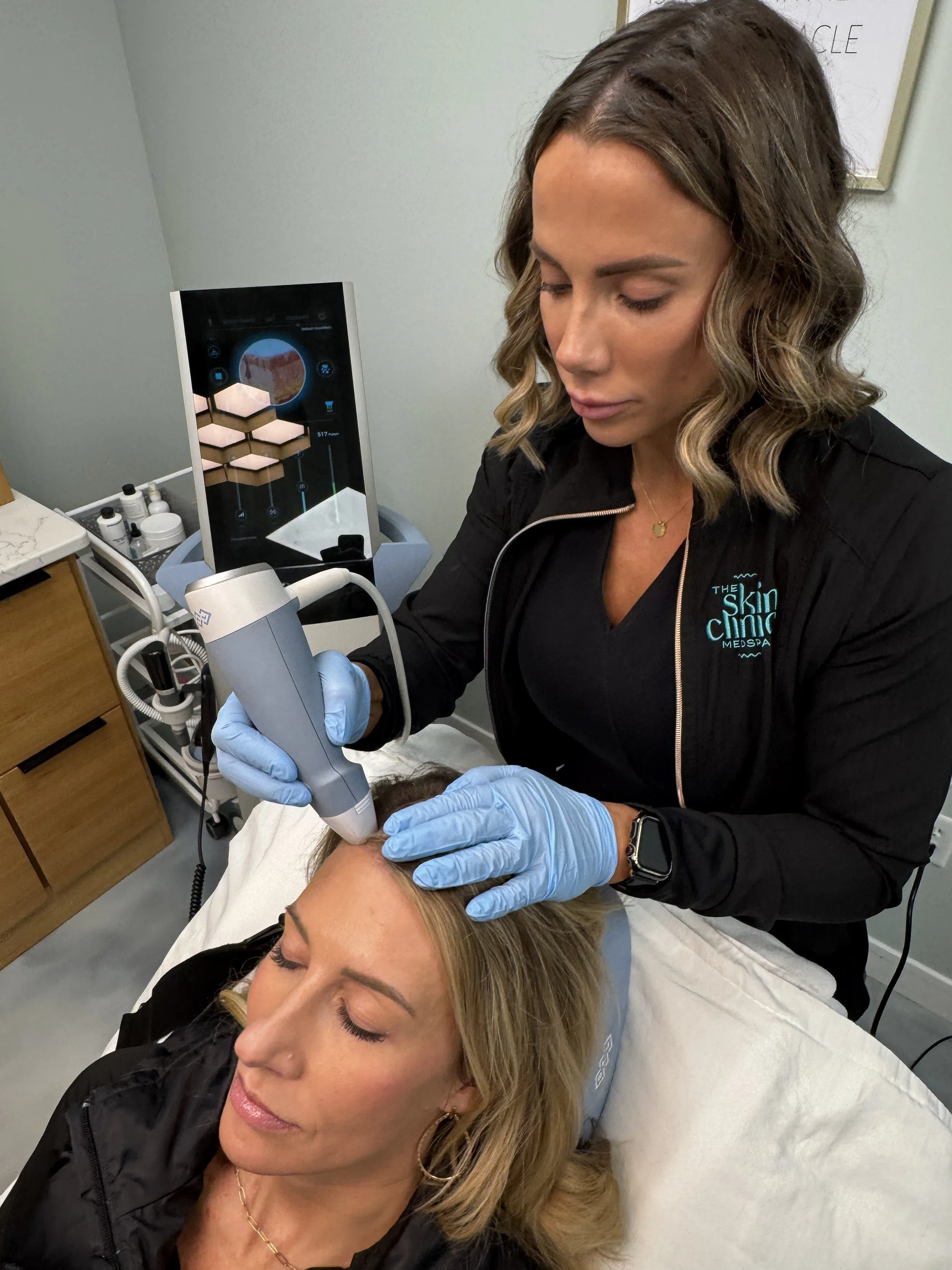 A woman receiving a cosmetic treatment on her forehead from a skincare professional at a clinic.