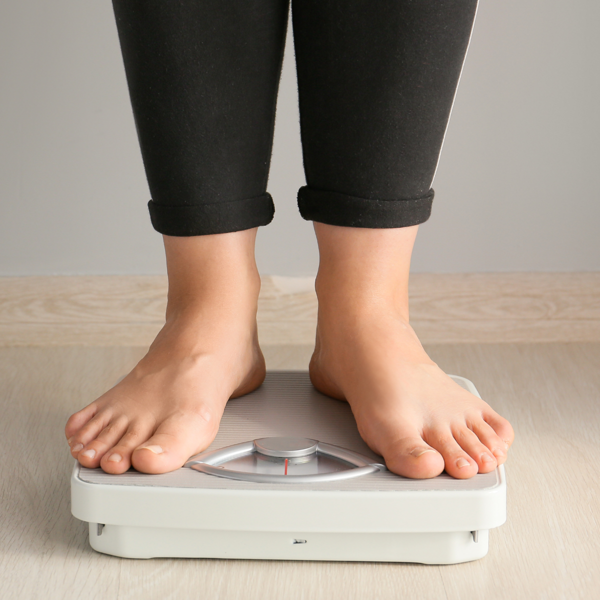 Person standing barefoot on a weighing scale indoors, focused on their feet and the scale.
