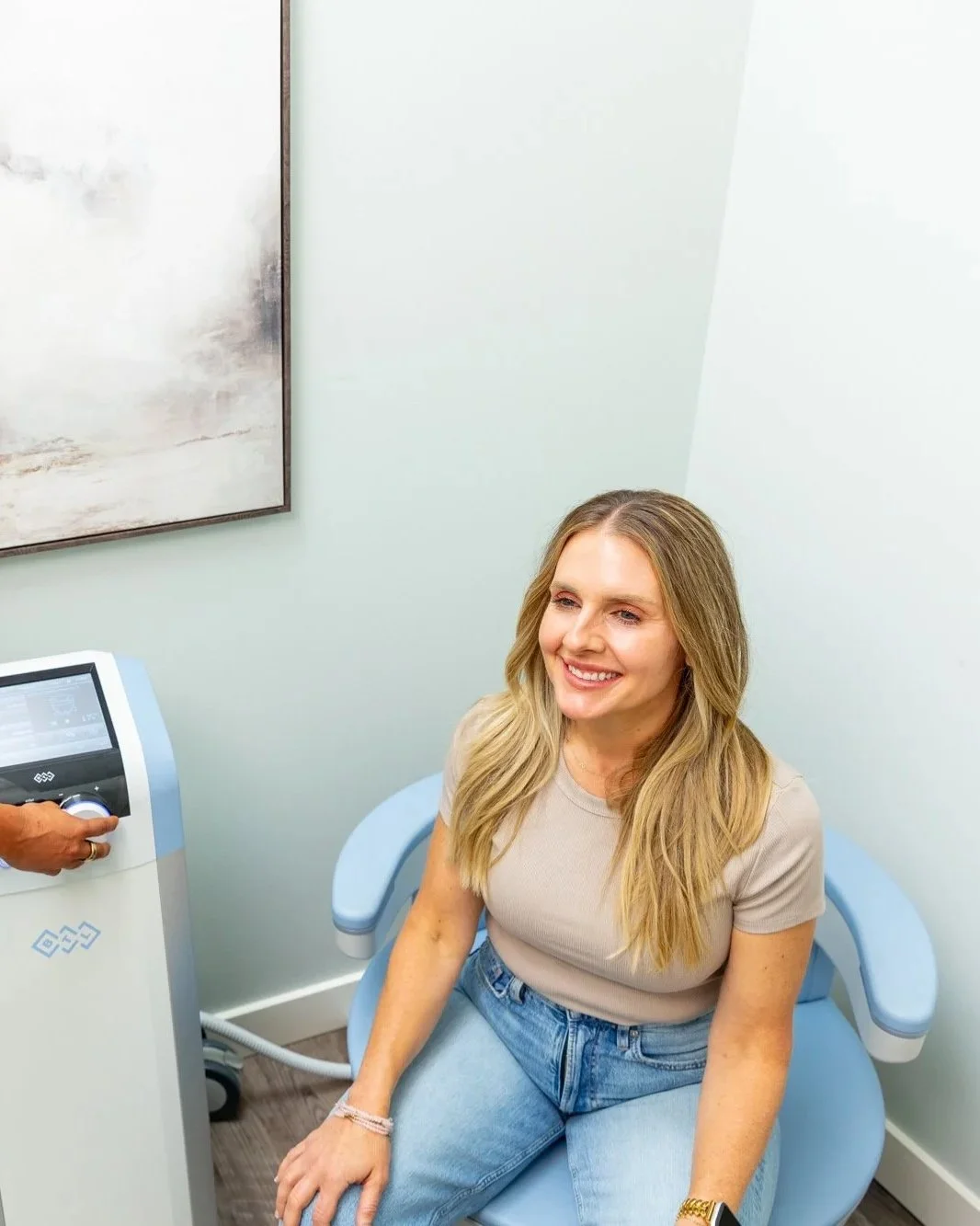 A woman smiling while sitting in a medical examination chair in a doctor's office.