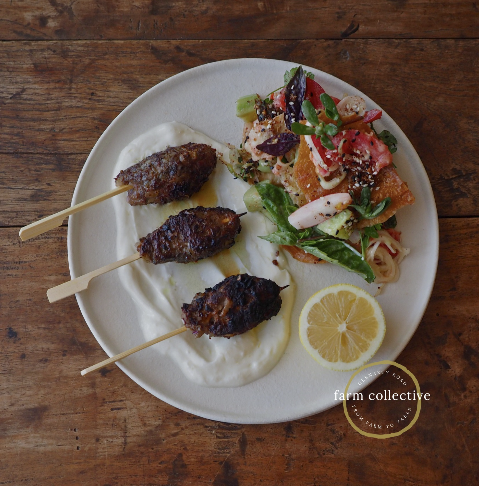 Three lamb kofta skewers over lemon labneh alongside a colourful farm garden salad on a ceramic plate