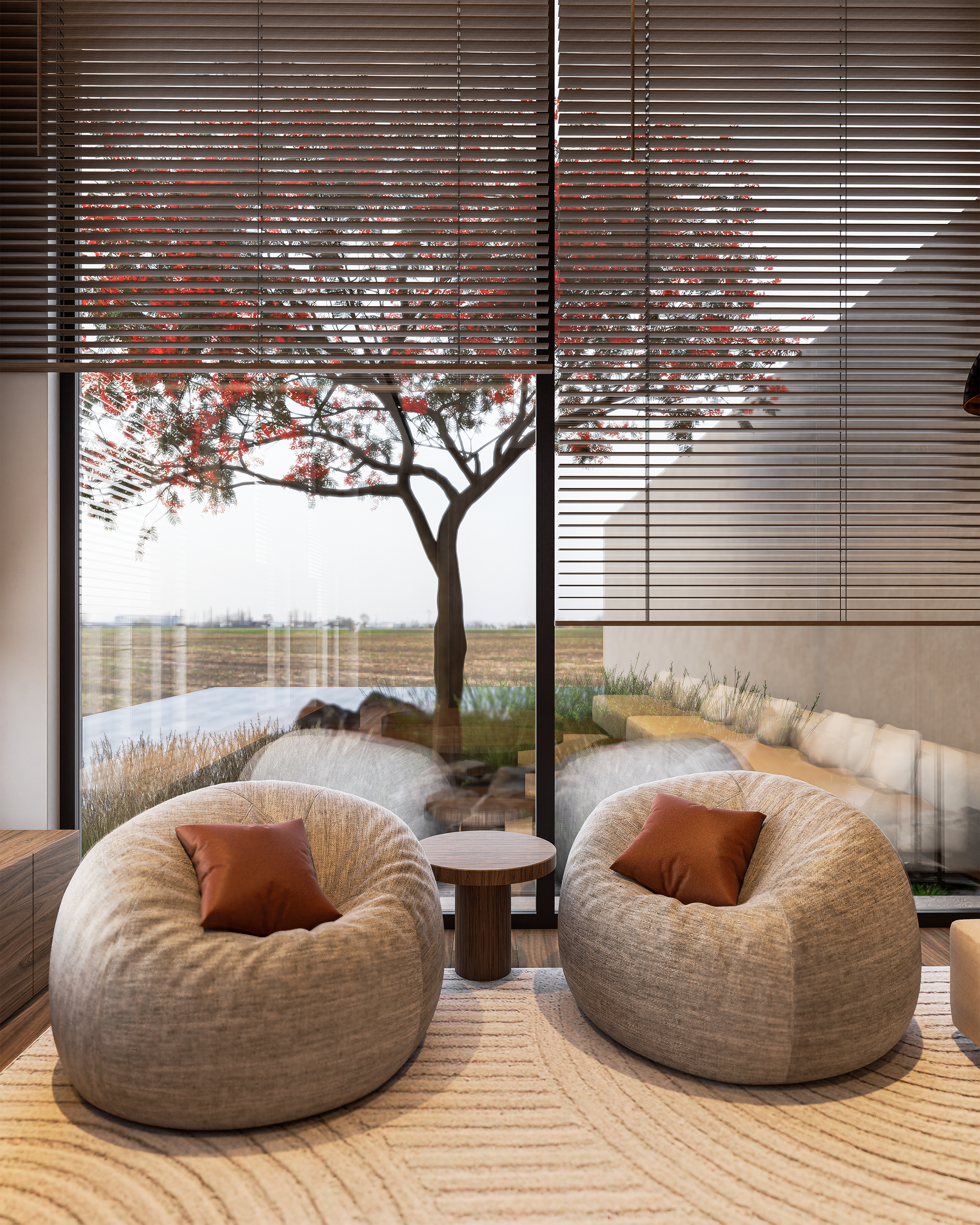 Living room with two large, beige, rounded armchairs with brown pillows, a small round wooden side table between them, a large window with wooden blinds showing a tree outside, and a light-colored rug with a curved pattern.