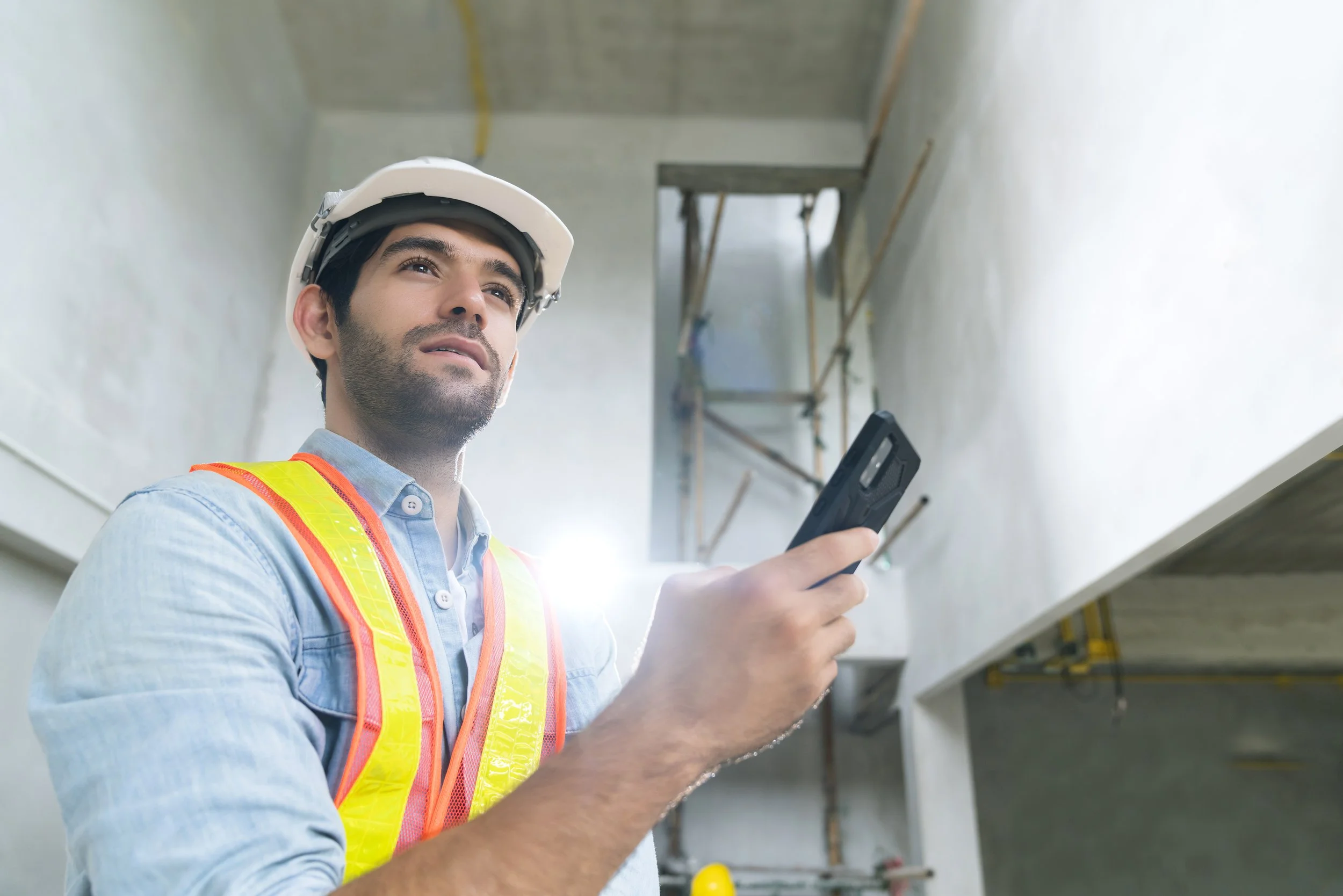 retrato-de-un-joven-ingeniero-caucasico-con-uniforme-y-casco-que-usa-la-mano-en-la-comunicacion-inteligente-en-el-fondo-de-la-construccion-d.jpg