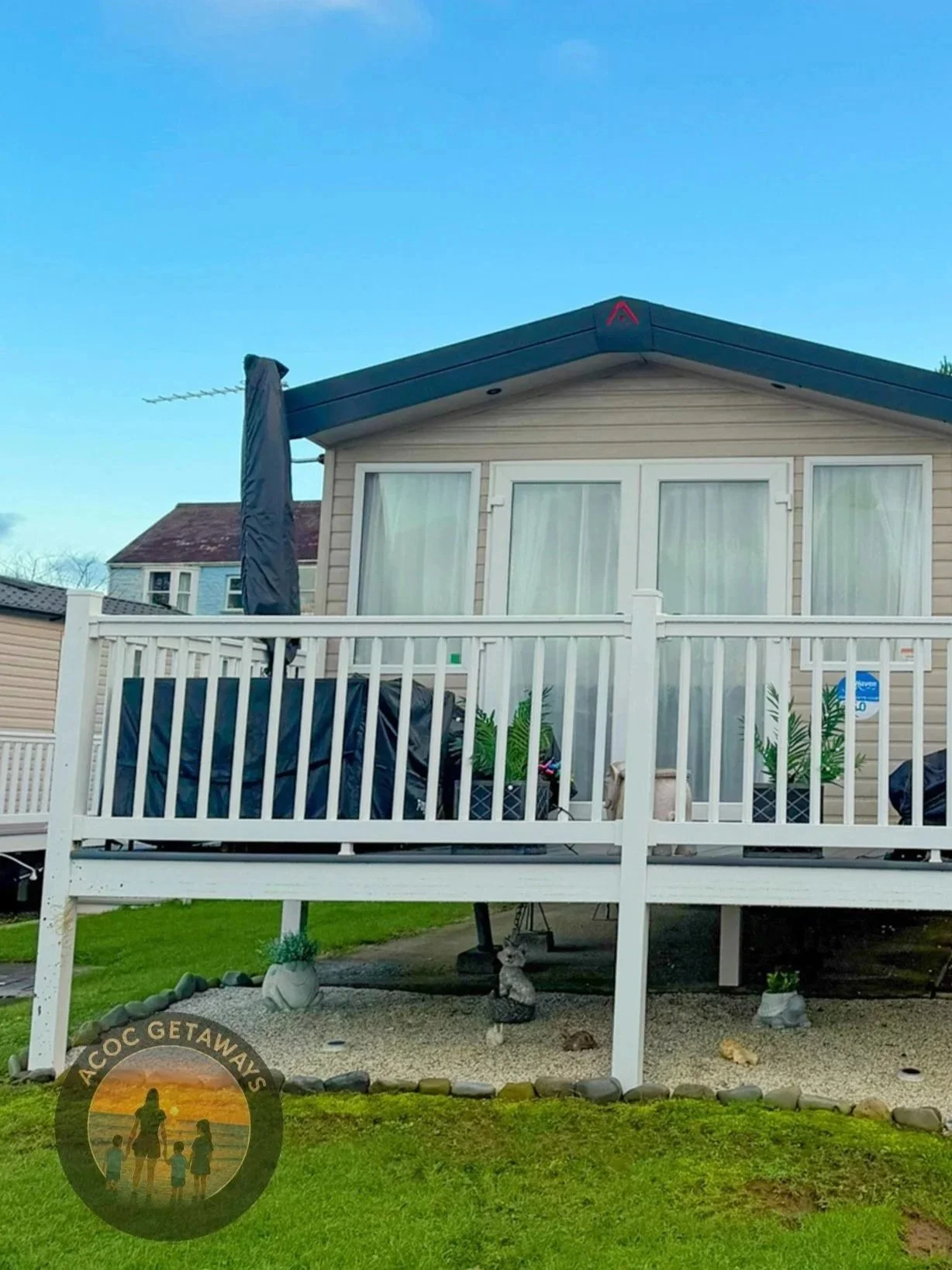 Front view of a house with a balcony, decorated with potted plants and garden ornaments, beneath a blue sky.