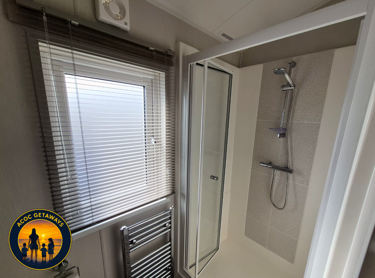 Bathroom with a window covered by blinds, a chrome towel rack, and a corner shower with a glass door and a handheld showerhead mounted on the wall.