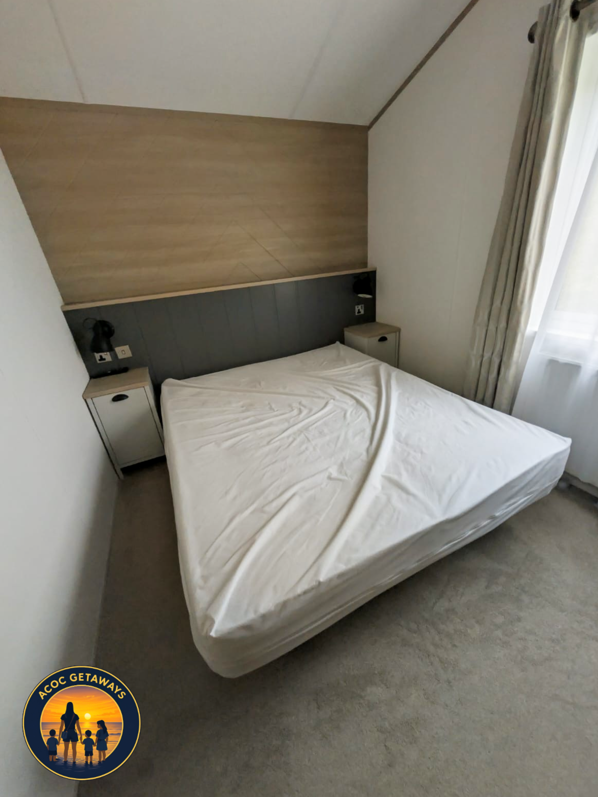 A bedroom with a bed, two nightstands, wall-mounted lamps, a wooden headboard, curtains, and a window.