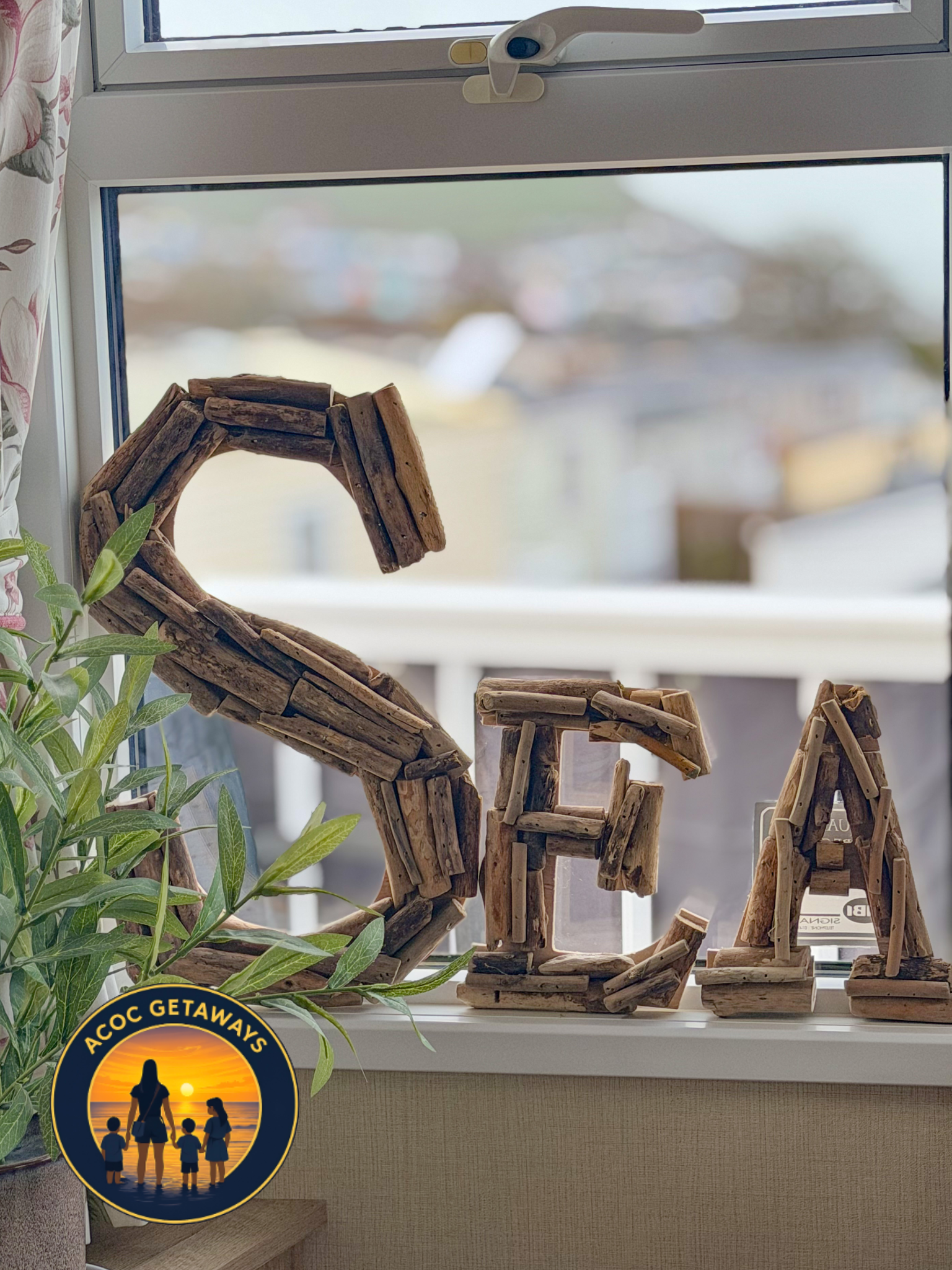Decorative wooden word cutout spelling 'LOVE' on a windowsill, with a plant nearby and a sunset scene sticker on the bottom left corner.