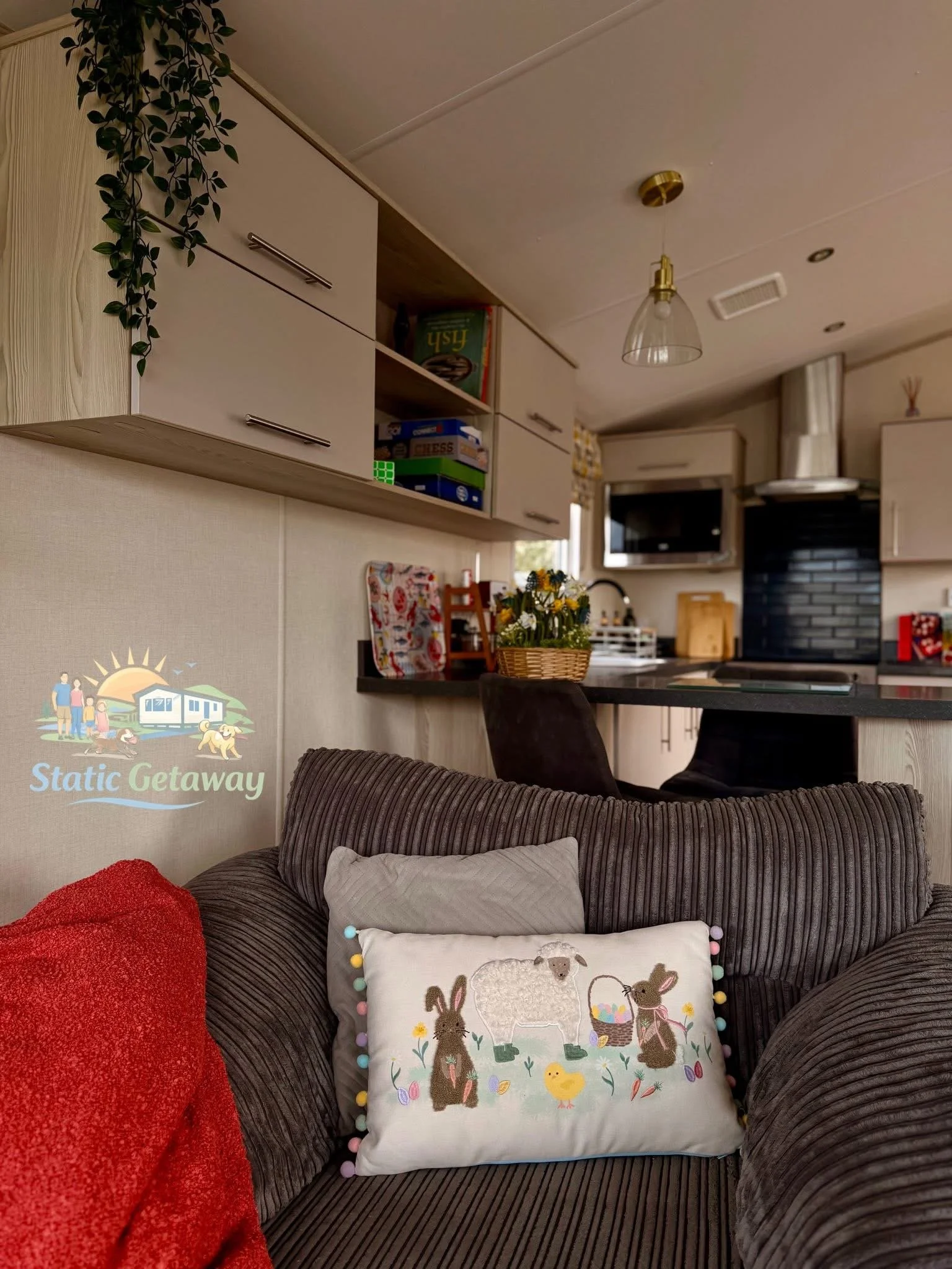 Decorative pillow with bunnies and chicks on a brown sofa, next to a red blanket and a white pillow, in a cozy living room.