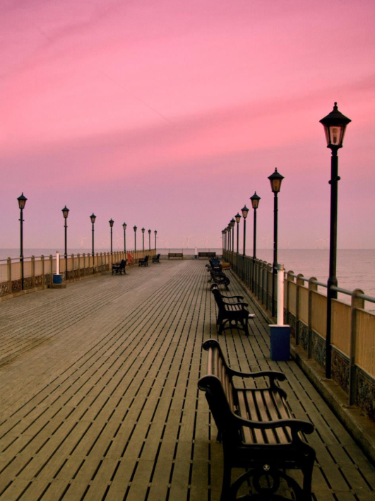 Empty pier with benches and lamp posts during sunset with pink sky