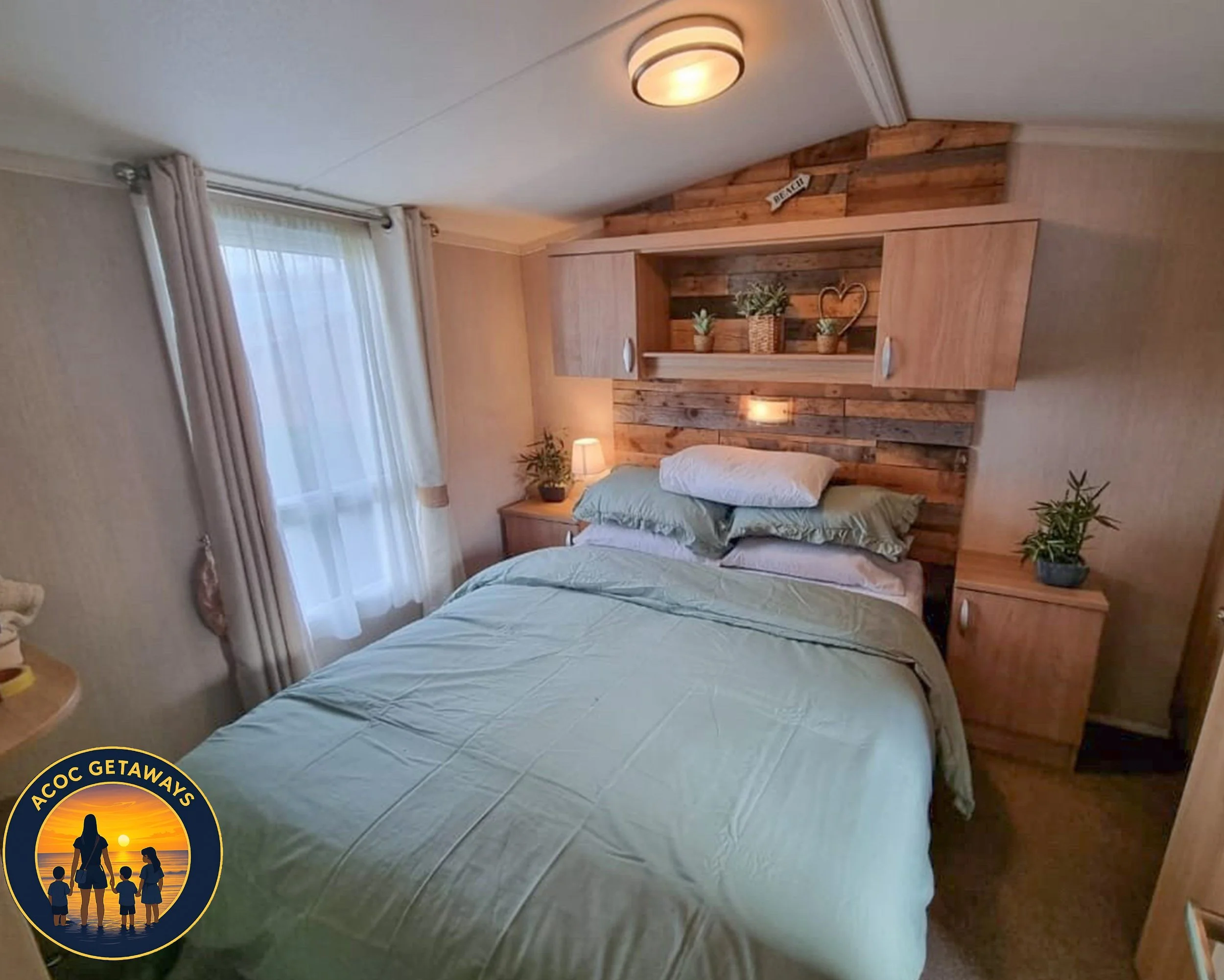 A cozy bedroom with a bed covered in light green sheets and multiple pillows against a wooden headboard. The headboard features a decorative wood panel with potted plants and a heart-shaped ornament. There are nightstands on both sides of the bed wit