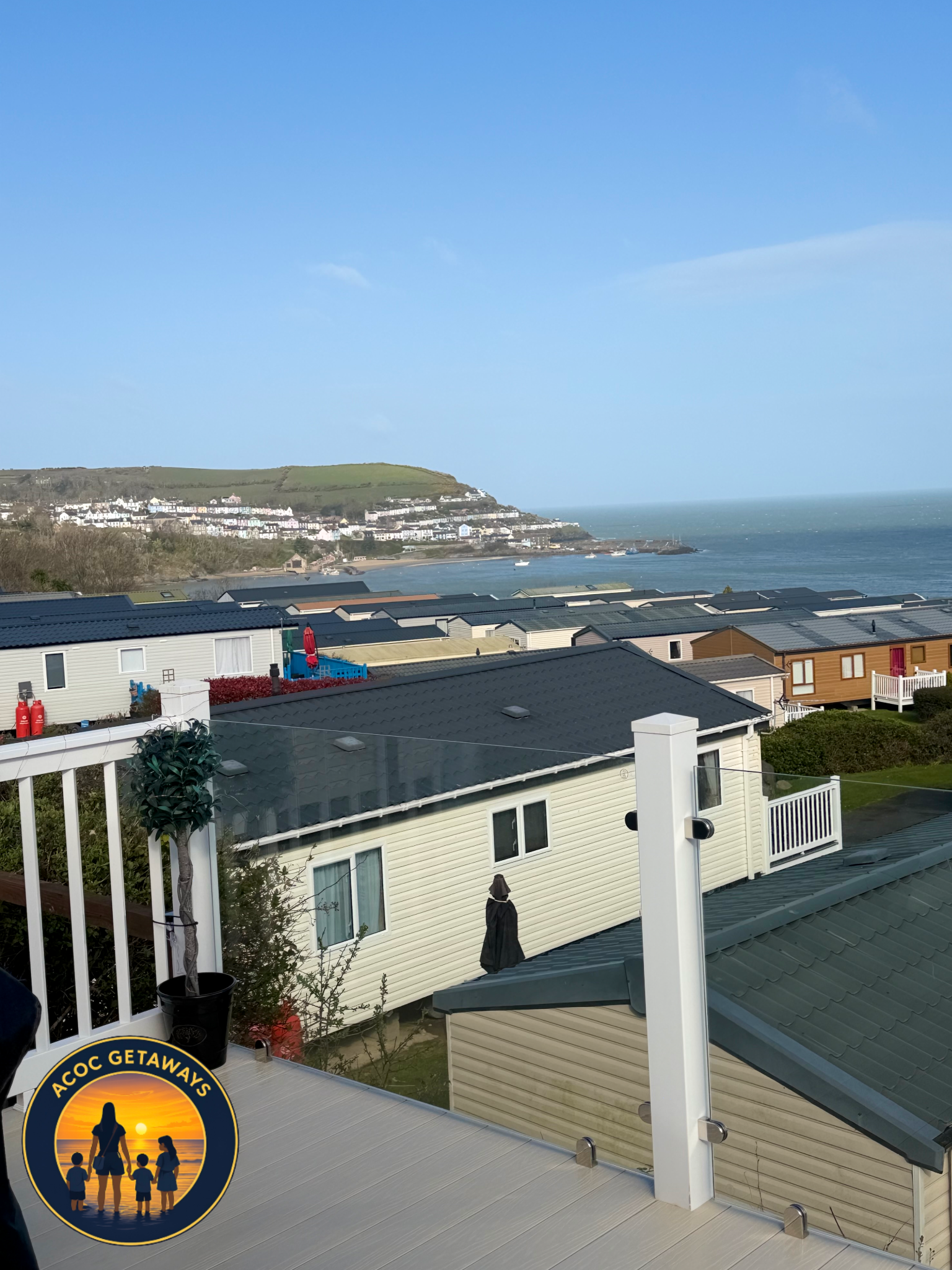 View from a balcony looking out over a coastal neighborhood with houses, a beach, and the ocean under a clear blue sky.