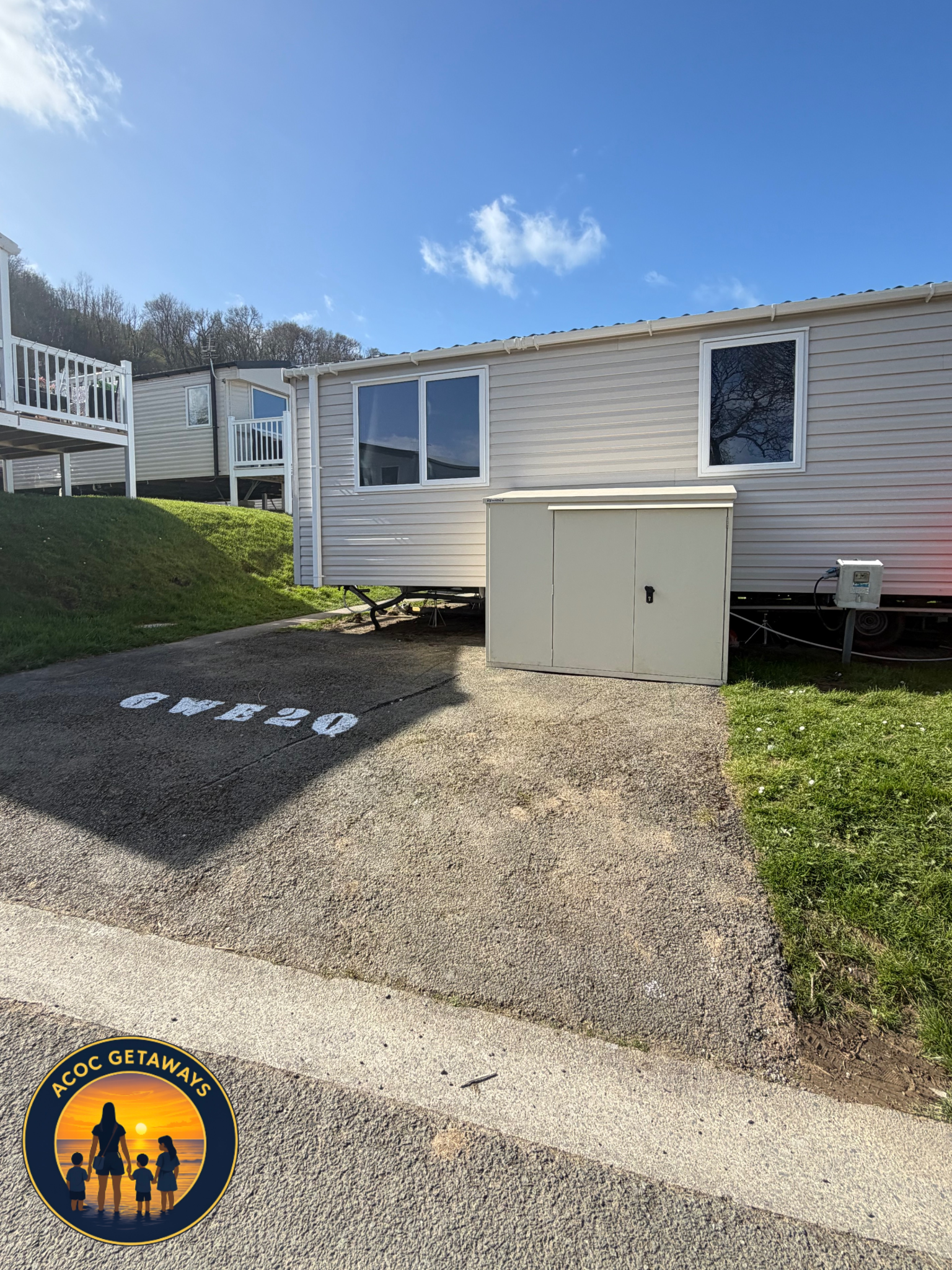 Mobile home with small storage shed, painted street number 40, in sunny weather with blue sky and some clouds.