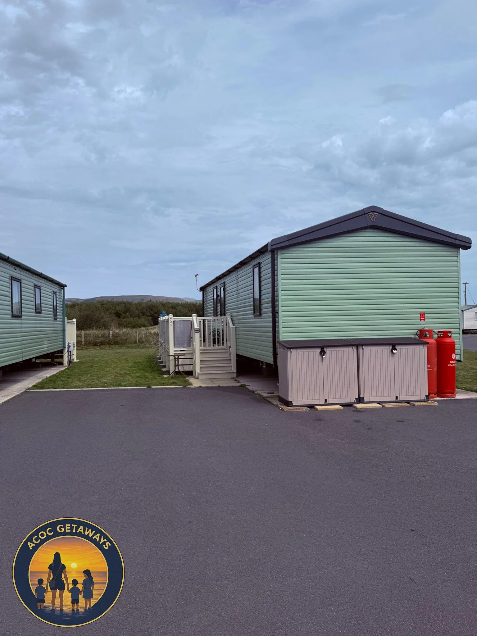 Mobile homes or RVs parked outdoors with a sunset and family logo sticker on the asphalt in the foreground.
