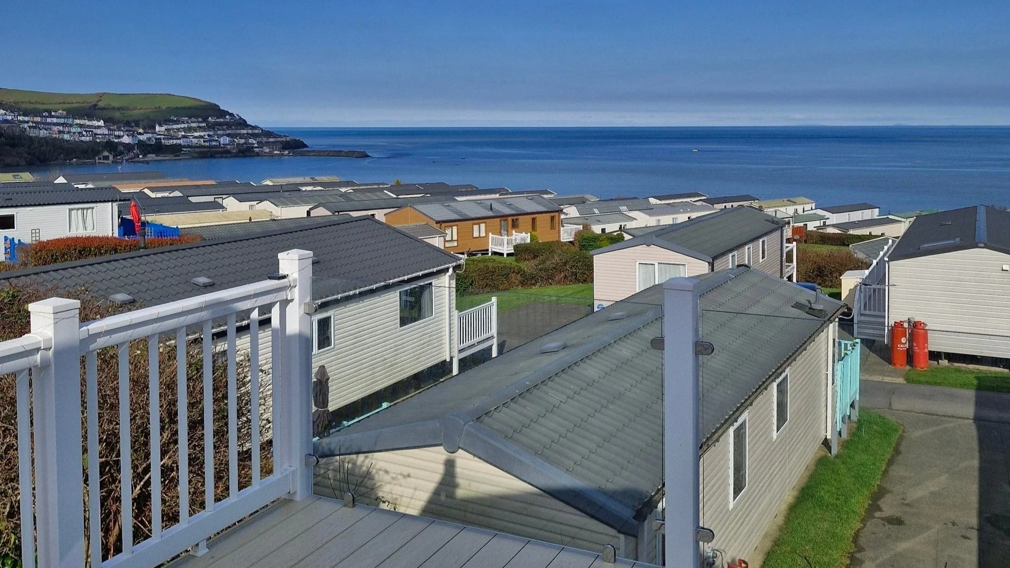 View of houses along a hillside overlooking a body of water, with blue skies overhead.
