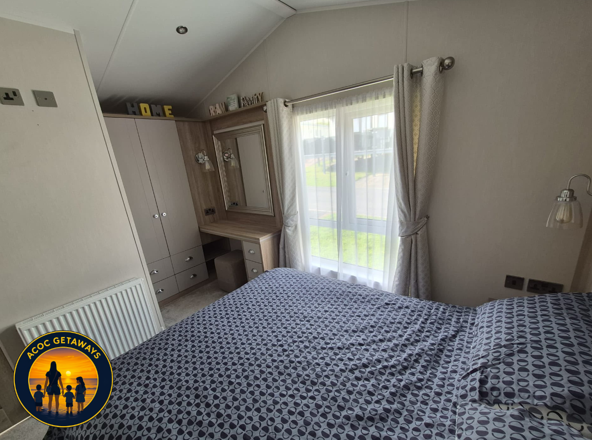 Bedroom with bed covered in blue and white patterned bedding, window with sheer curtains and heavy drapes, built-in wardrobe with mirror, small vanity with mirror, and decorative letters spelling 'HOME' on top.