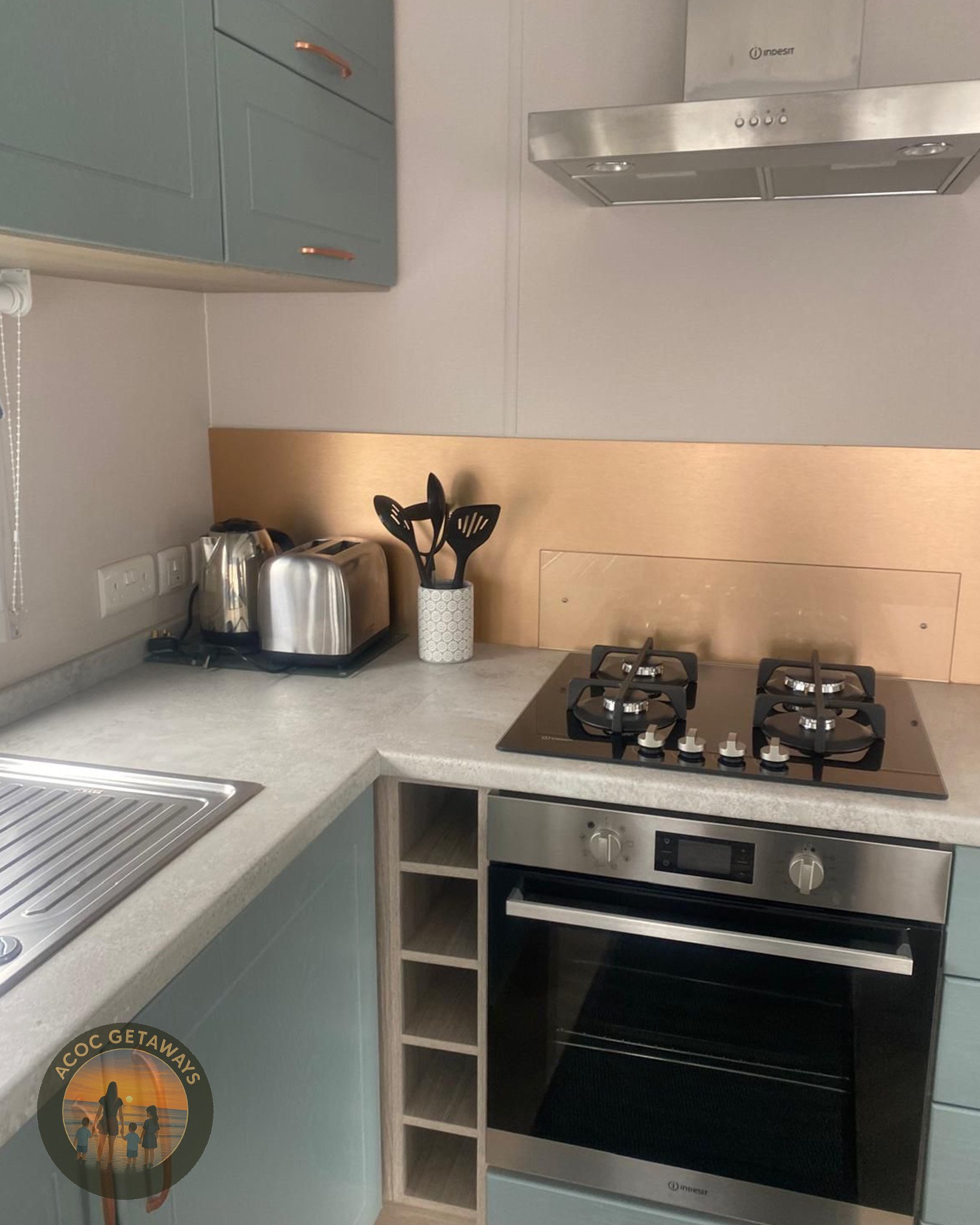 Kitchen with a stovetop, oven, toaster, kettle, and utensil holder on the countertop near a wall with electrical outlets.