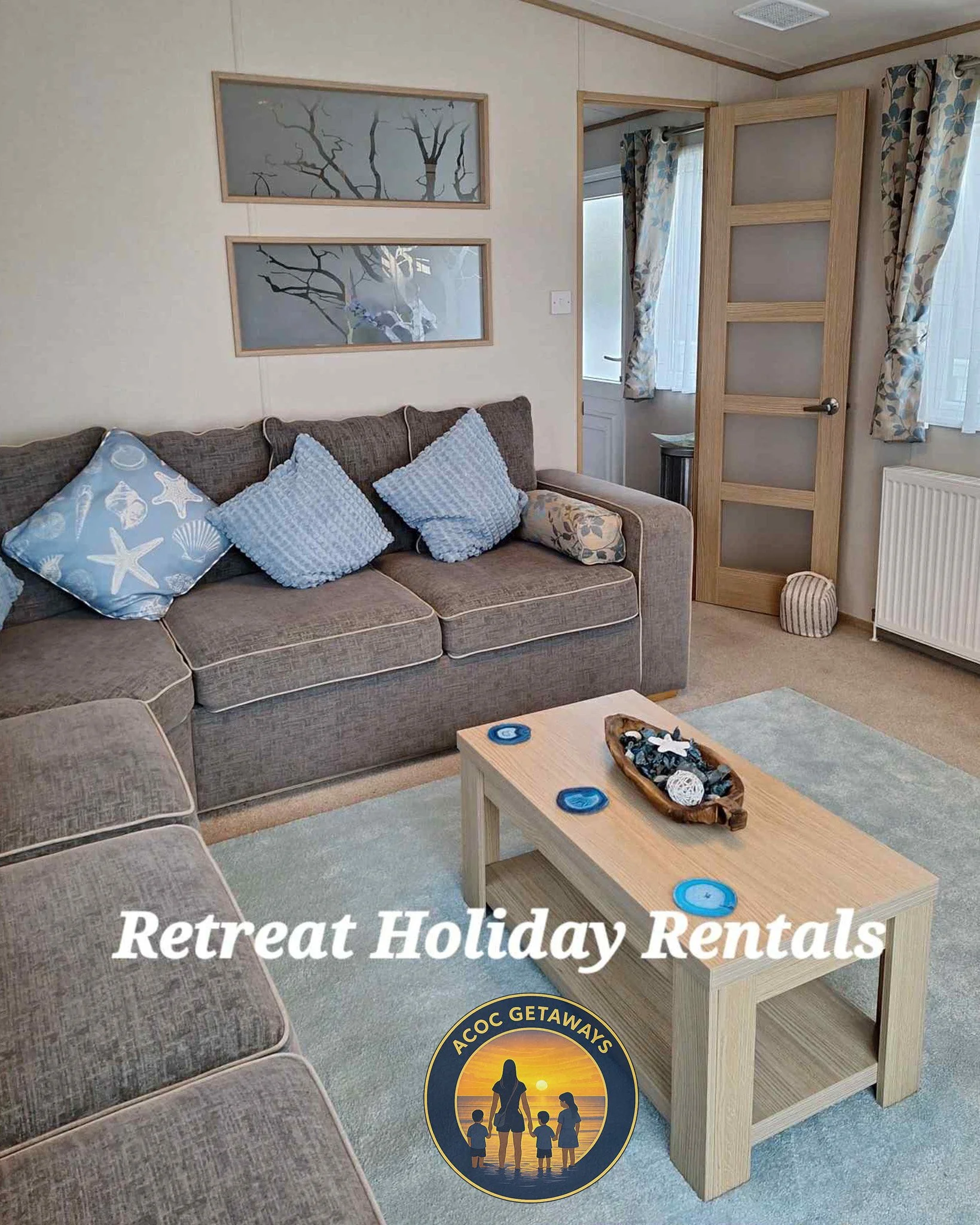 Living room with gray sofa, blue pillows, wooden coffee table, wall art, curtains, window, and door, promoting retreat holiday rentals by ACOK Getaways.