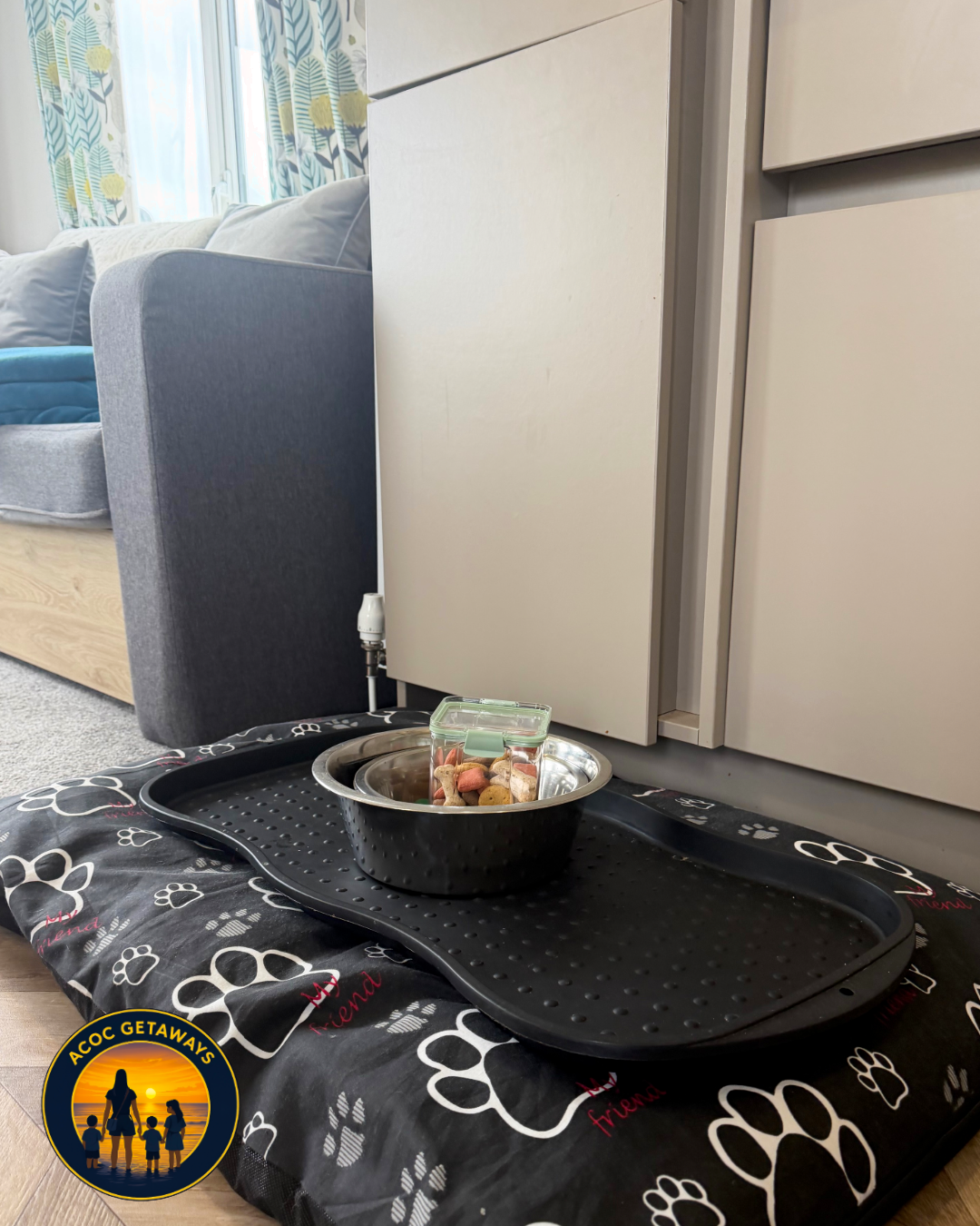 A dog food bowl filled with dry dog food, placed on a black mat with paw print pattern, on a blanket with paw print and the words 'best friend'.