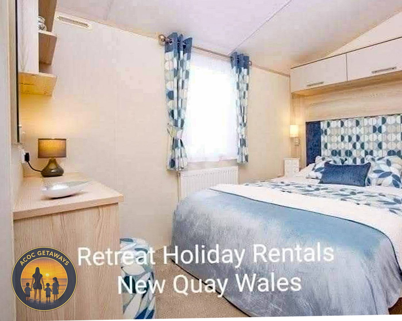 A cozy hotel bedroom with a large bed, blue bedding, and matching curtains. There is a nightstand with a lamp on each side of the bed, and a window with white curtains allowing natural light to brighten the room. The decor features a blue, white, and beige color scheme.