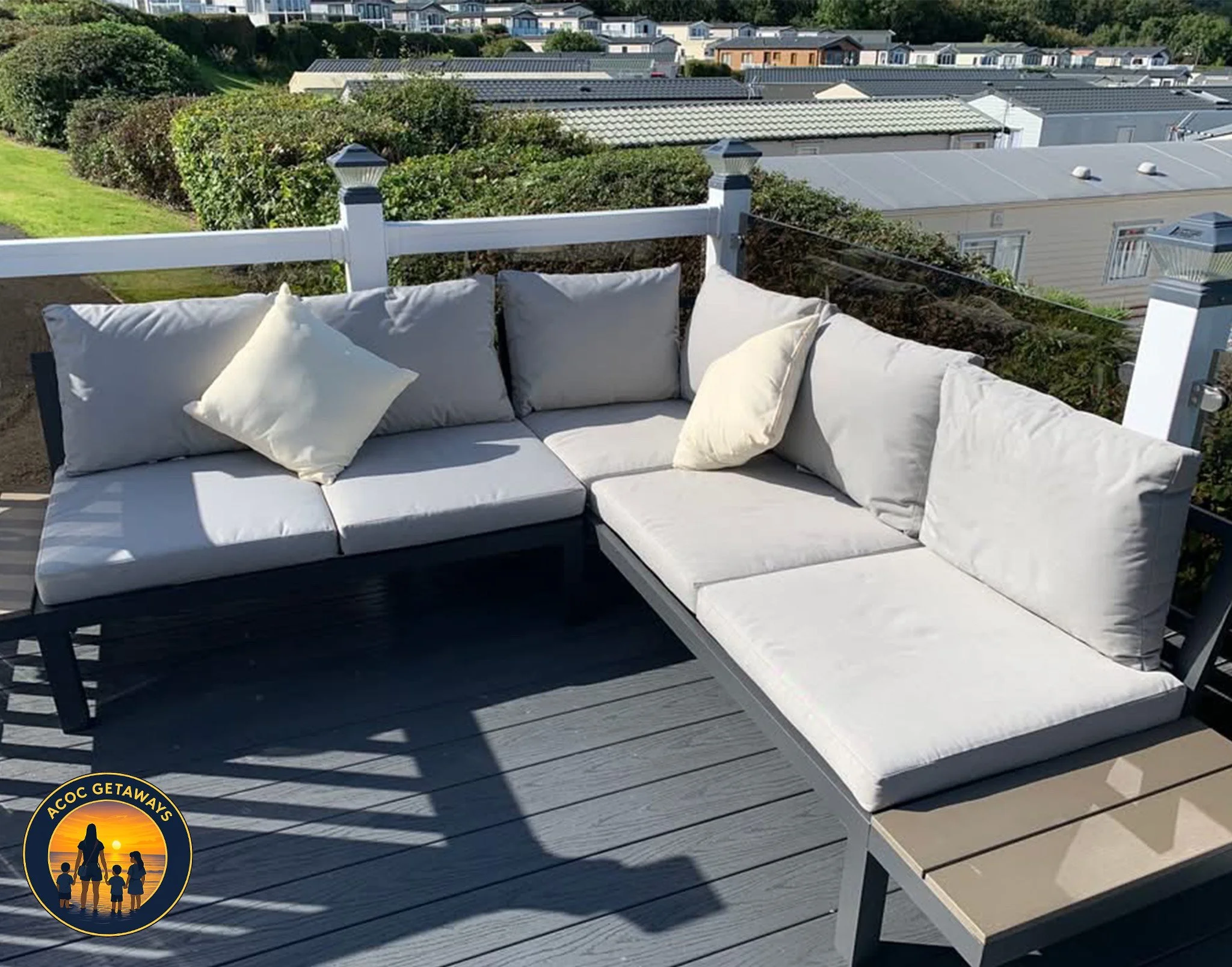 Outdoor sectional sofa with white cushions on a wooden deck, overlooking a residential area with houses and greenery.