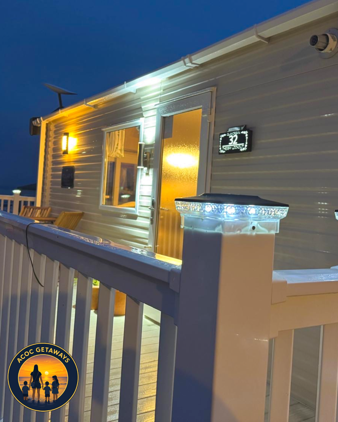 A cozy mobile home decorated with warm yellow and white lights, seen from a balcony with a white railing illuminated with LED lights, at dusk.