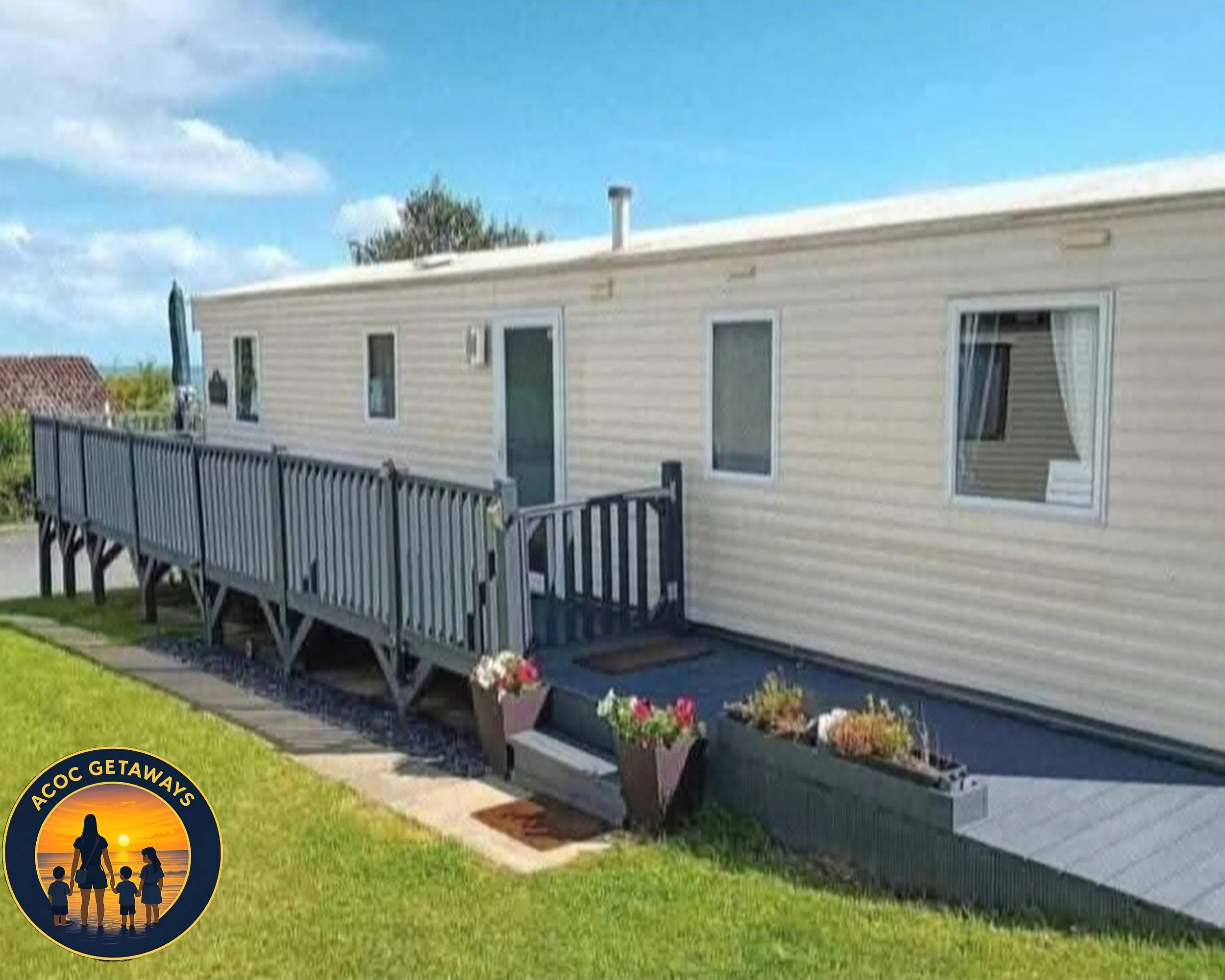 Mobile home with a small elevated porch and flowers in planters, set on a grassy area on a sunny day.