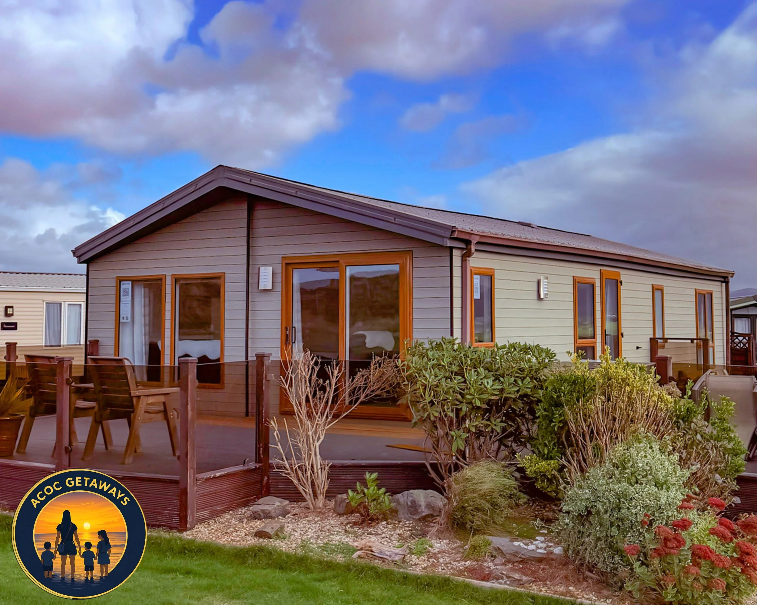 A small, modern house with wooden sliding glass doors and windows, surrounded by a garden with bushes and flowers, under a partly cloudy sky.