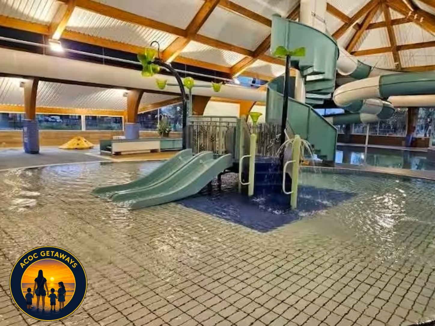 Indoor water park with multiple water slides, including two small slides and a larger spiral slide, set inside a wooden roof structure with skylights.