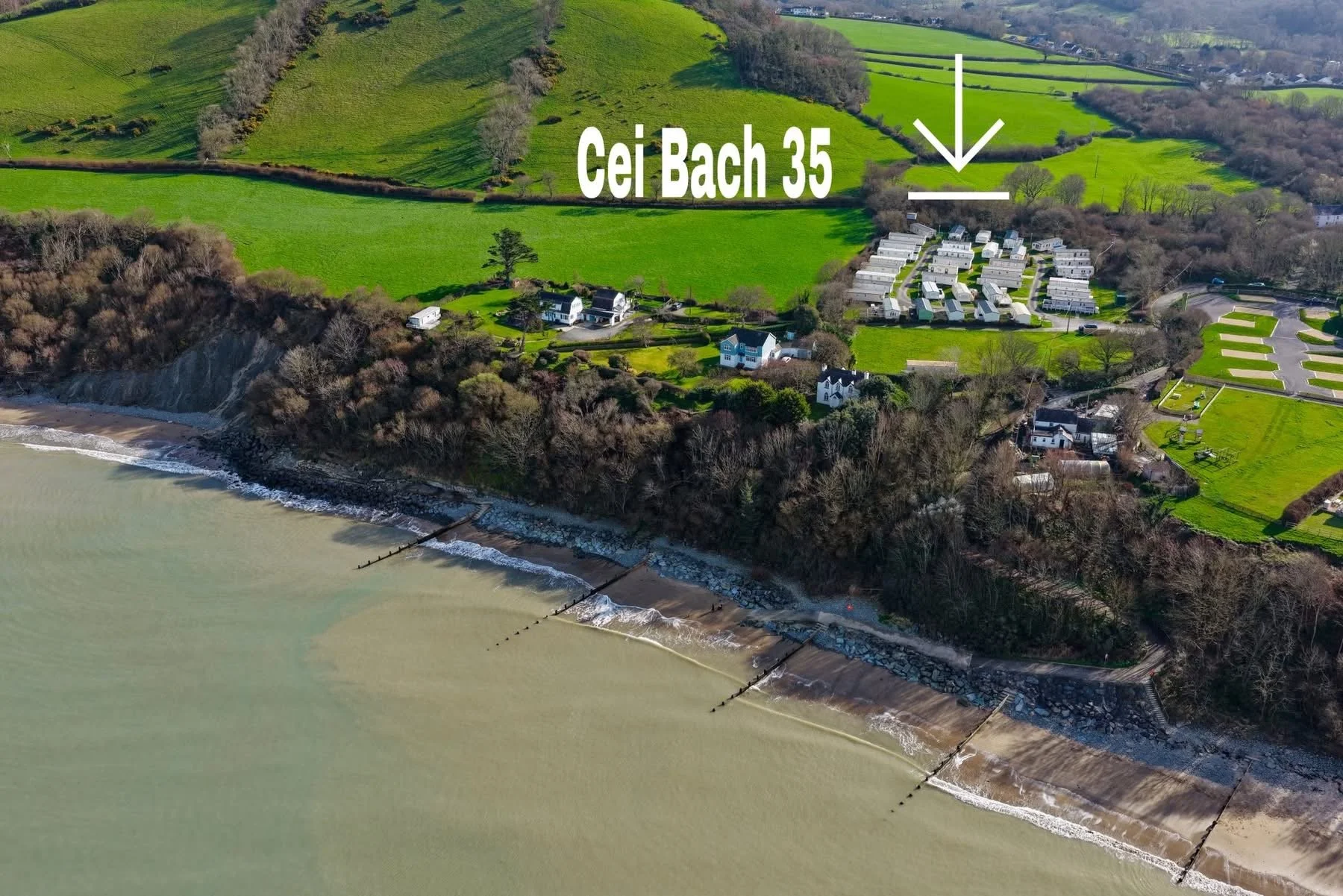 Aerial view of a coastal landscape with green hills, residential houses, and a beach with a seawall.