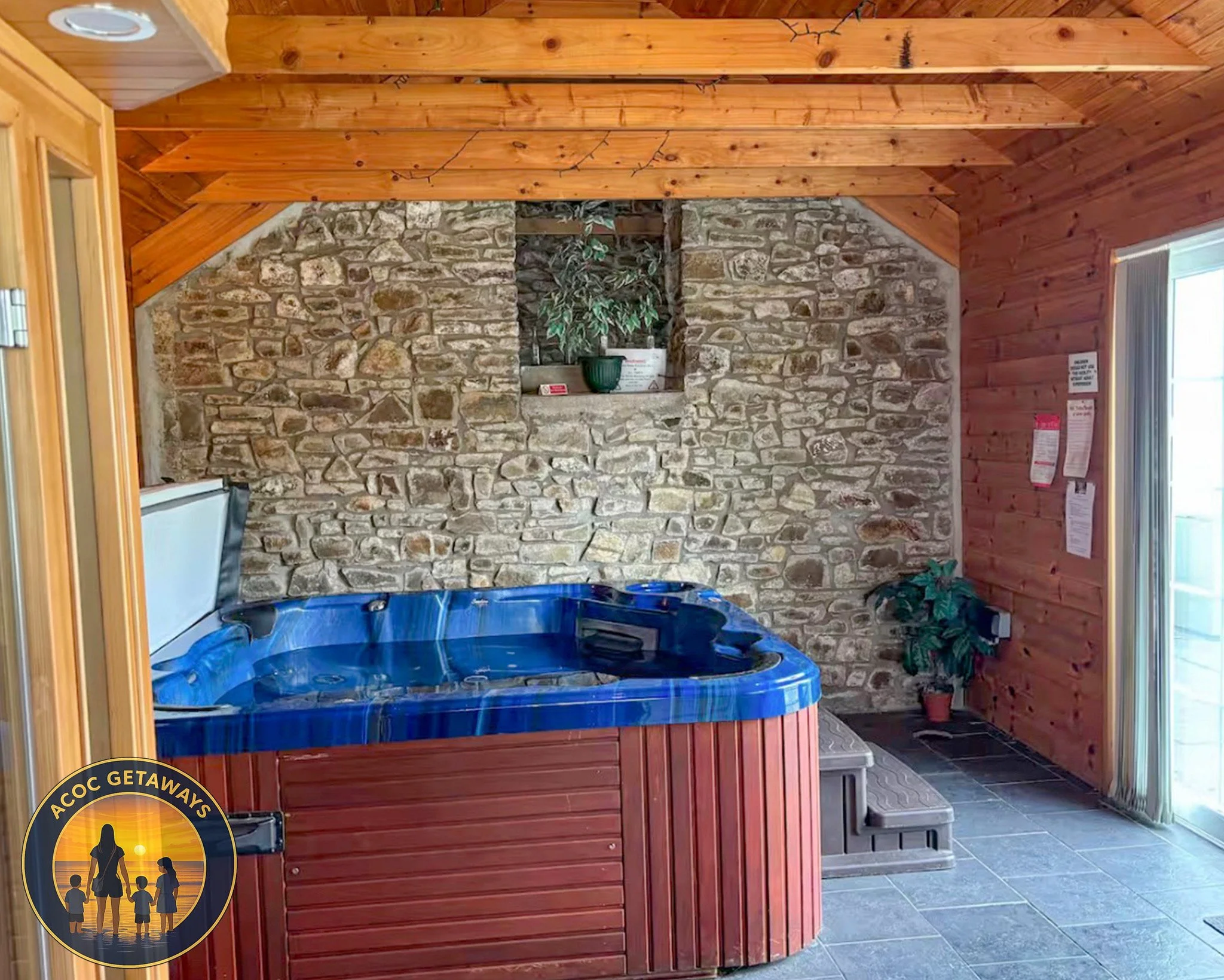 A small indoor pool with a blue cover, set against a stone wall with a small window shelf holding a potted plant and a white container. The room has wooden paneling on the walls and ceiling.