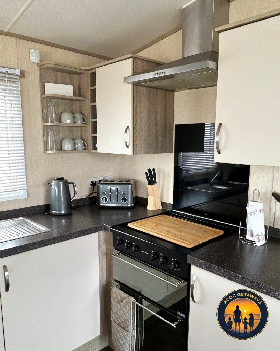 Kitchen with black countertop, white cabinets, stainless steel kettle and toaster, wooden cutting board, and black stove.