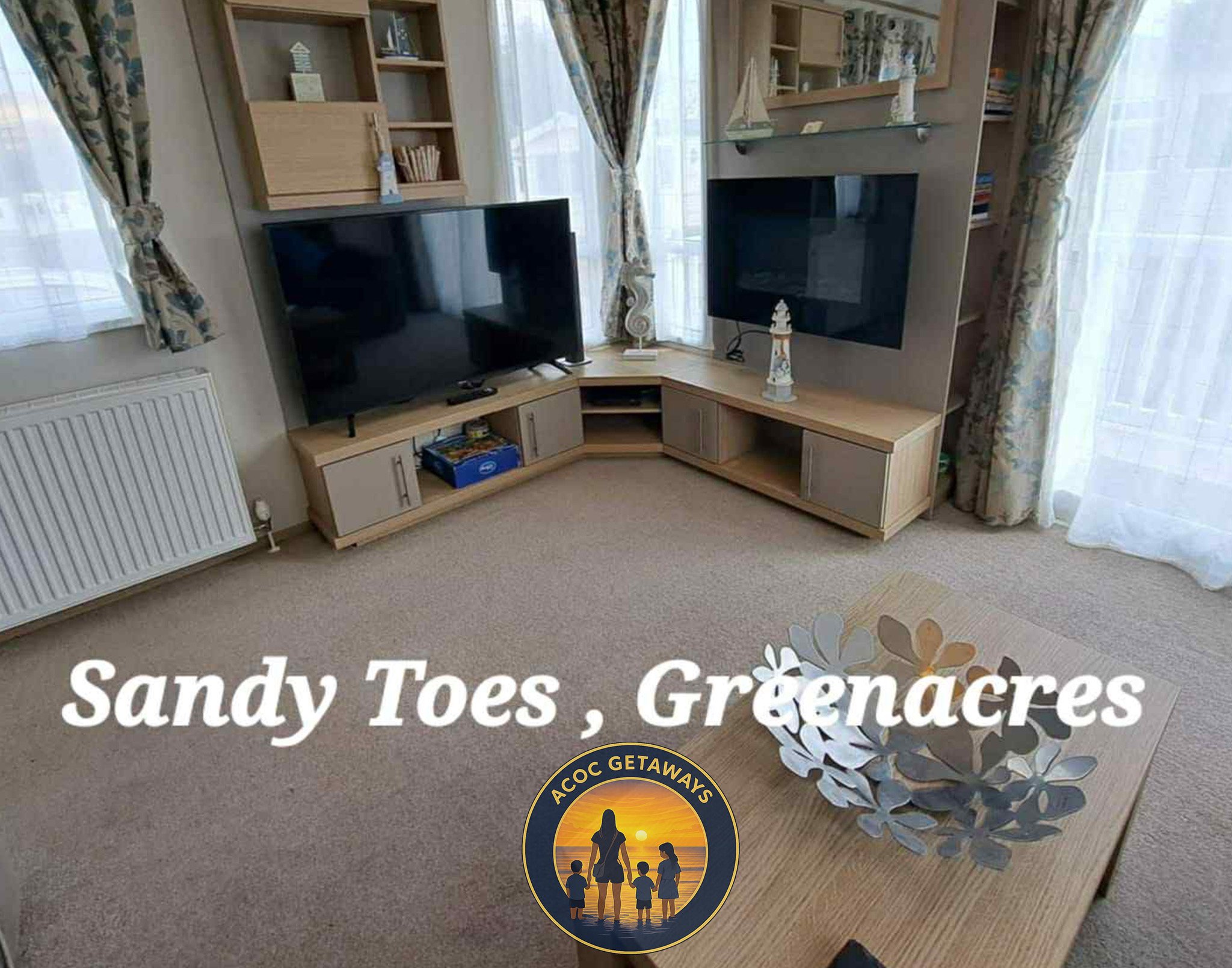 Living room with two large flat-screen TVs on a custom wooden entertainment unit, surrounded by bookshelves, with a coffee table in the foreground and floral curtains on large windows.