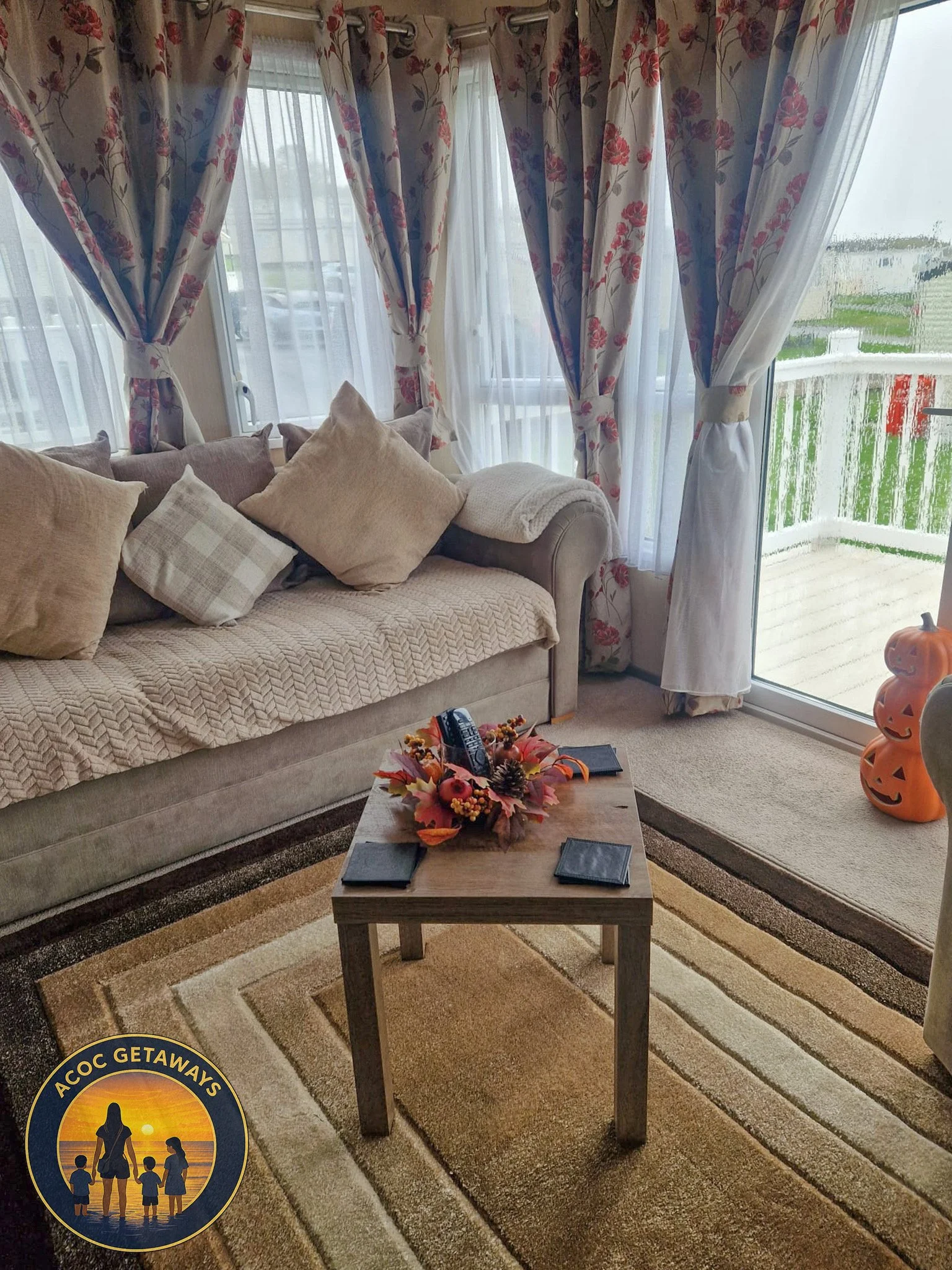 Living room with beige sofa, pillows, floral curtains, coffee table with fall decor, and Halloween pumpkin decorations.