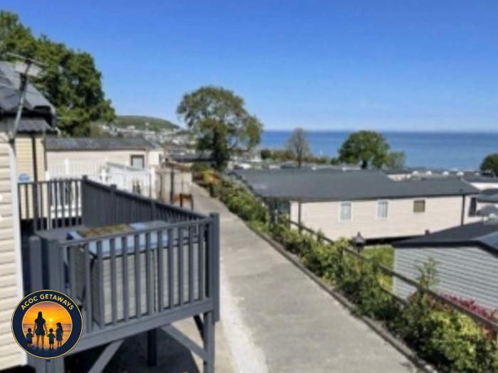 View of rooftops and trees overlooking the ocean from a balcony in a coastal area.